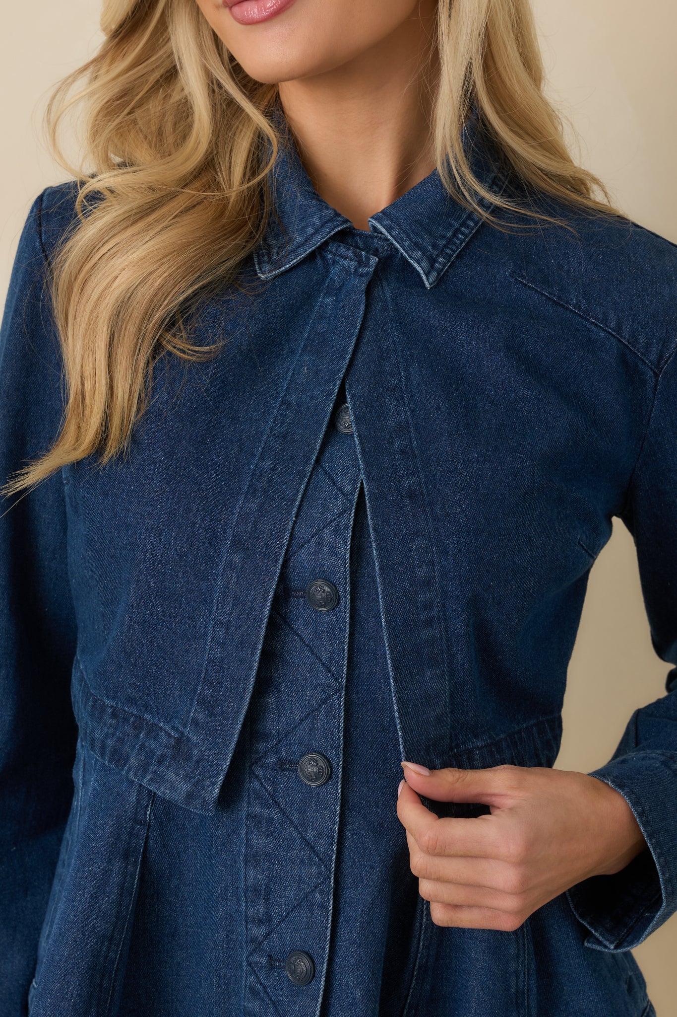 Close view of dark wash cotton denim fabric featuring sturdy stitching and front button hardware detail.