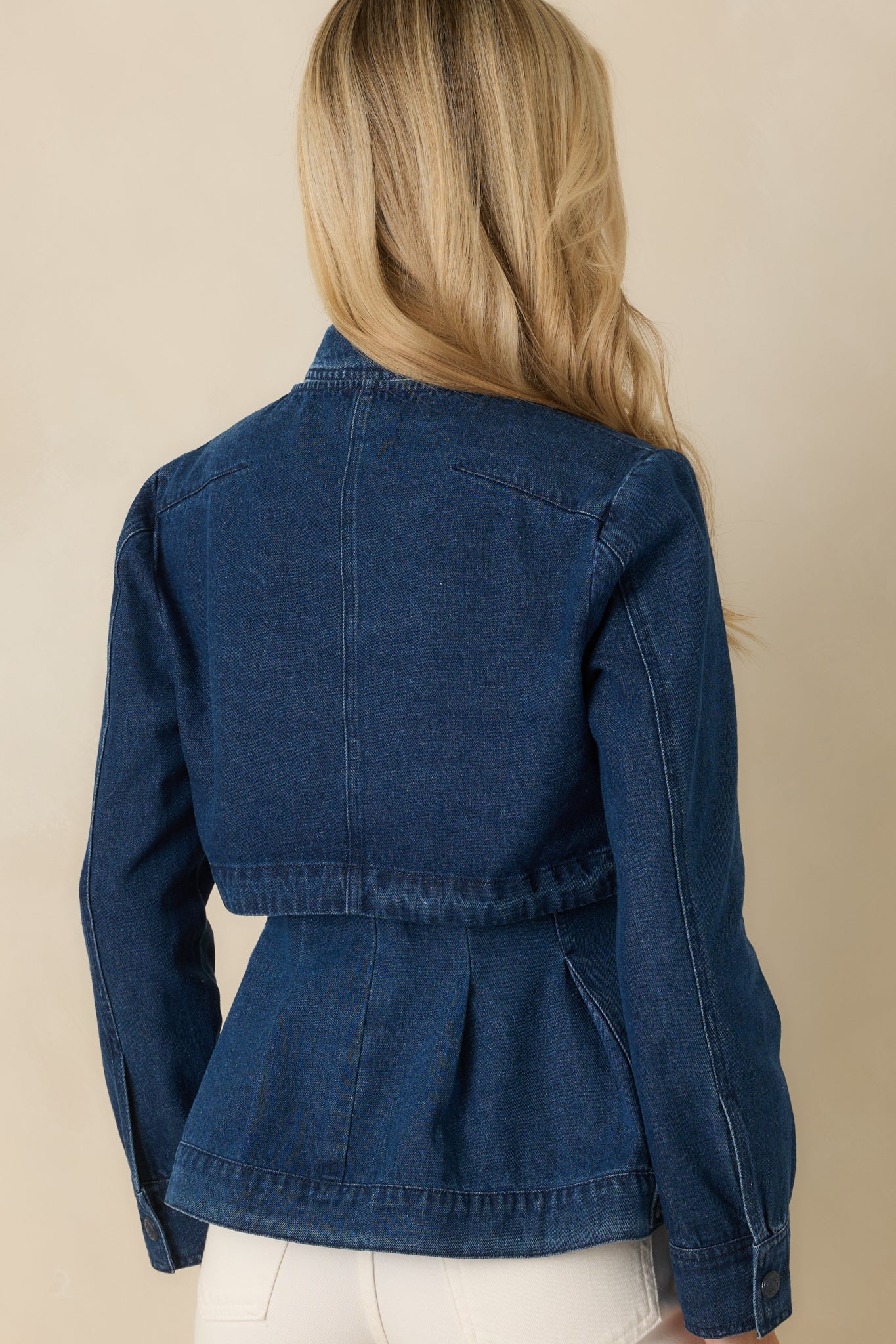 Dark wash cropped denim jacket displaying a clean rear silhouette with structured seaming and long sleeves.