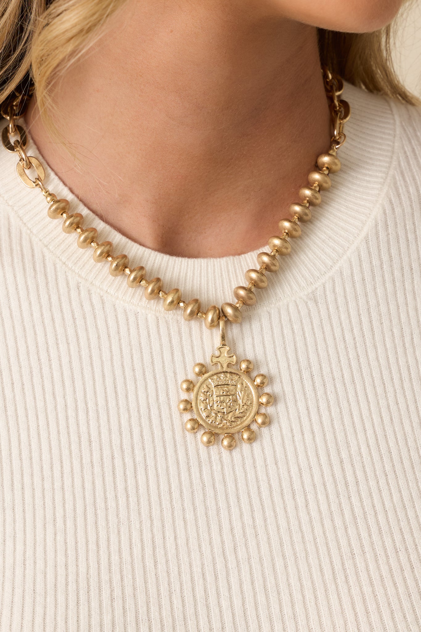 Detailed close-up of the gold medallion pendant showing the embossed crest, granulated border, and textured worn gold finish.