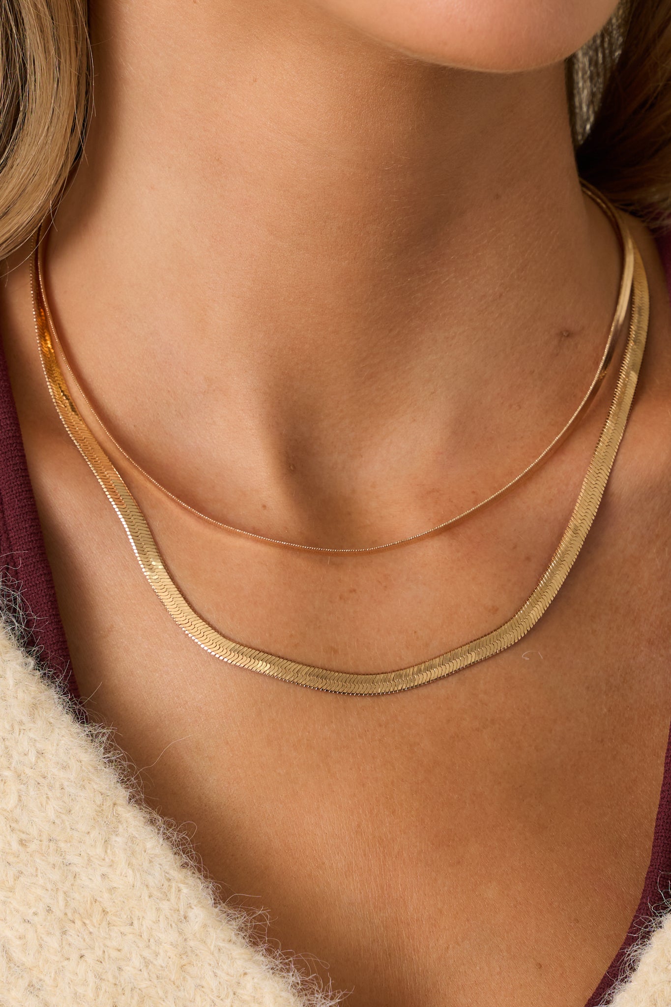 Detailed close-up of the herringbone chains and lobster clasp showing the polished gold finish and fine links.