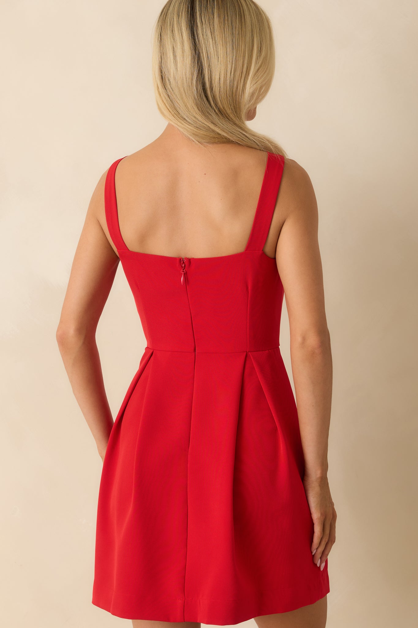 Rear view of the red mini dress highlighting the sleeveless silhouette and smooth pleated skirt.

