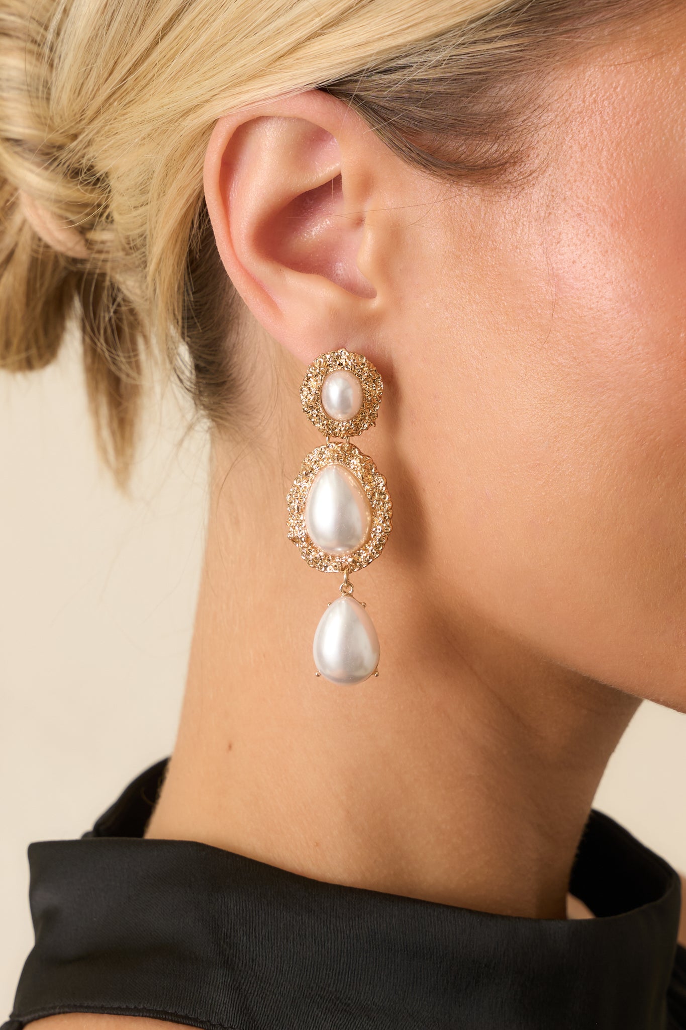 Detailed close-up of the gold earrings showing the textured oval bezels, centered faux pearls, and dangling teardrop pearl.