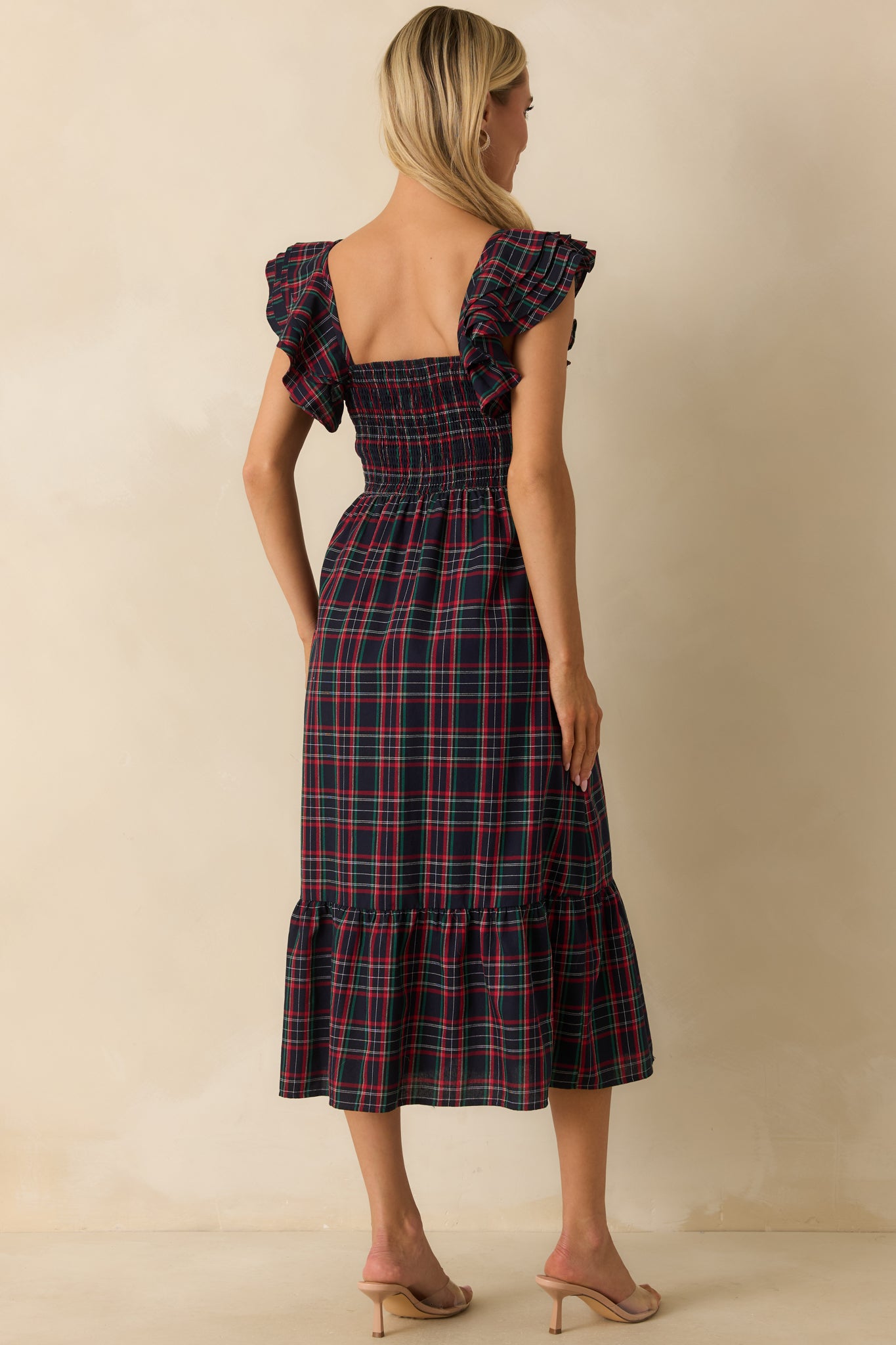 Rear view of navy plaid dress showing the smocked back, flutter sleeves, and tiered skirt layers.