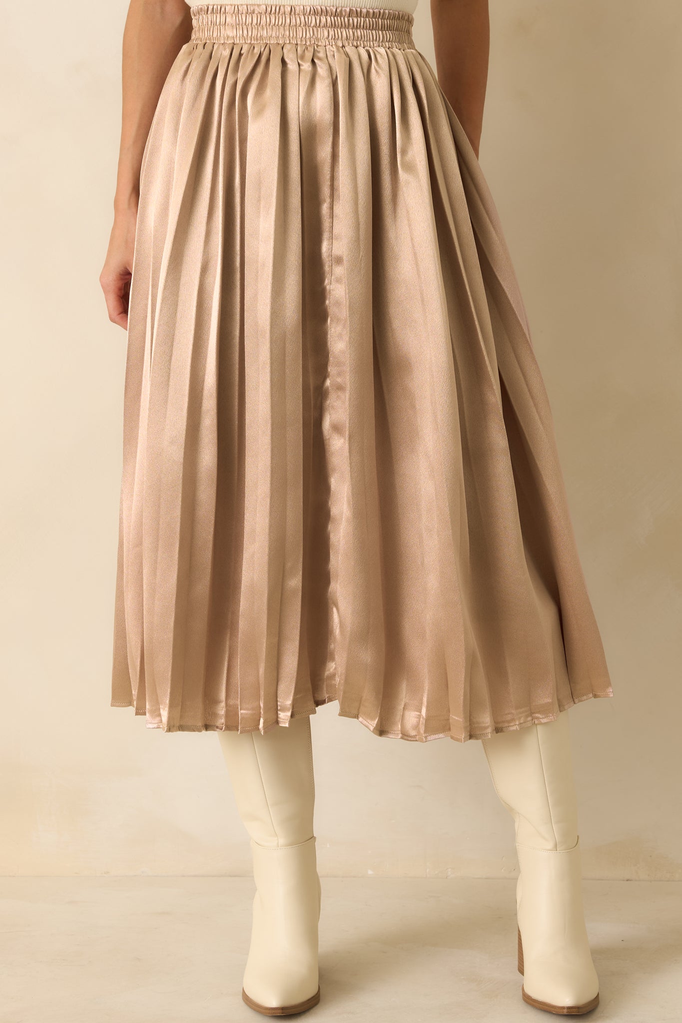 Crop highlighting the pleats and smooth rose gold texture of the midi skirt.
