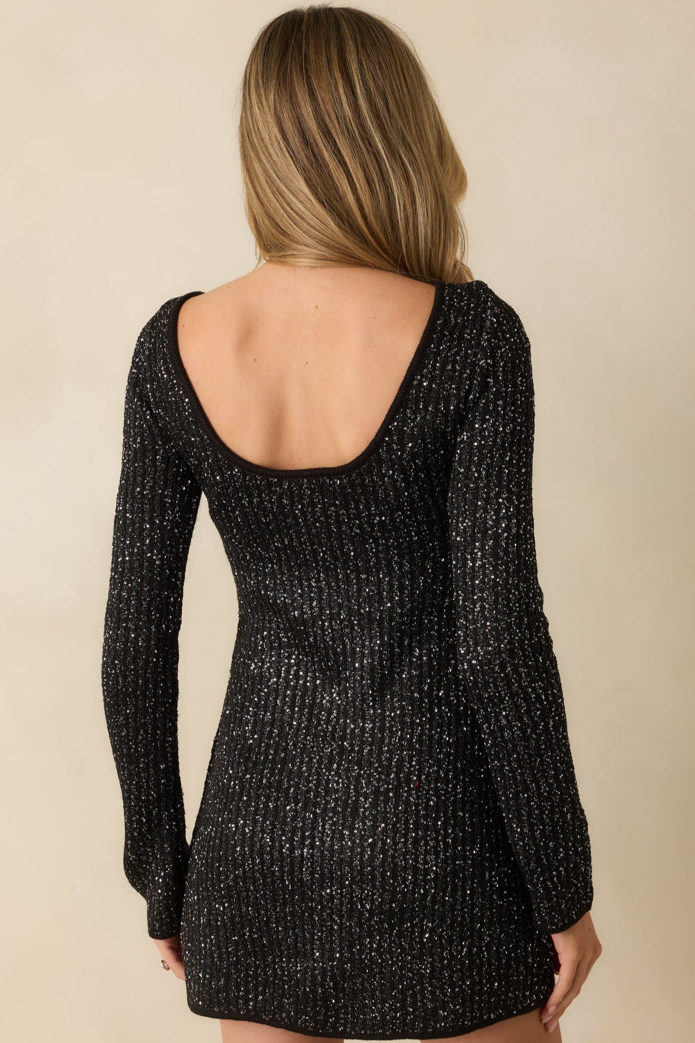 Rear view of the black mini dress featuring a scoop back and long sleeves with sequin accents.
