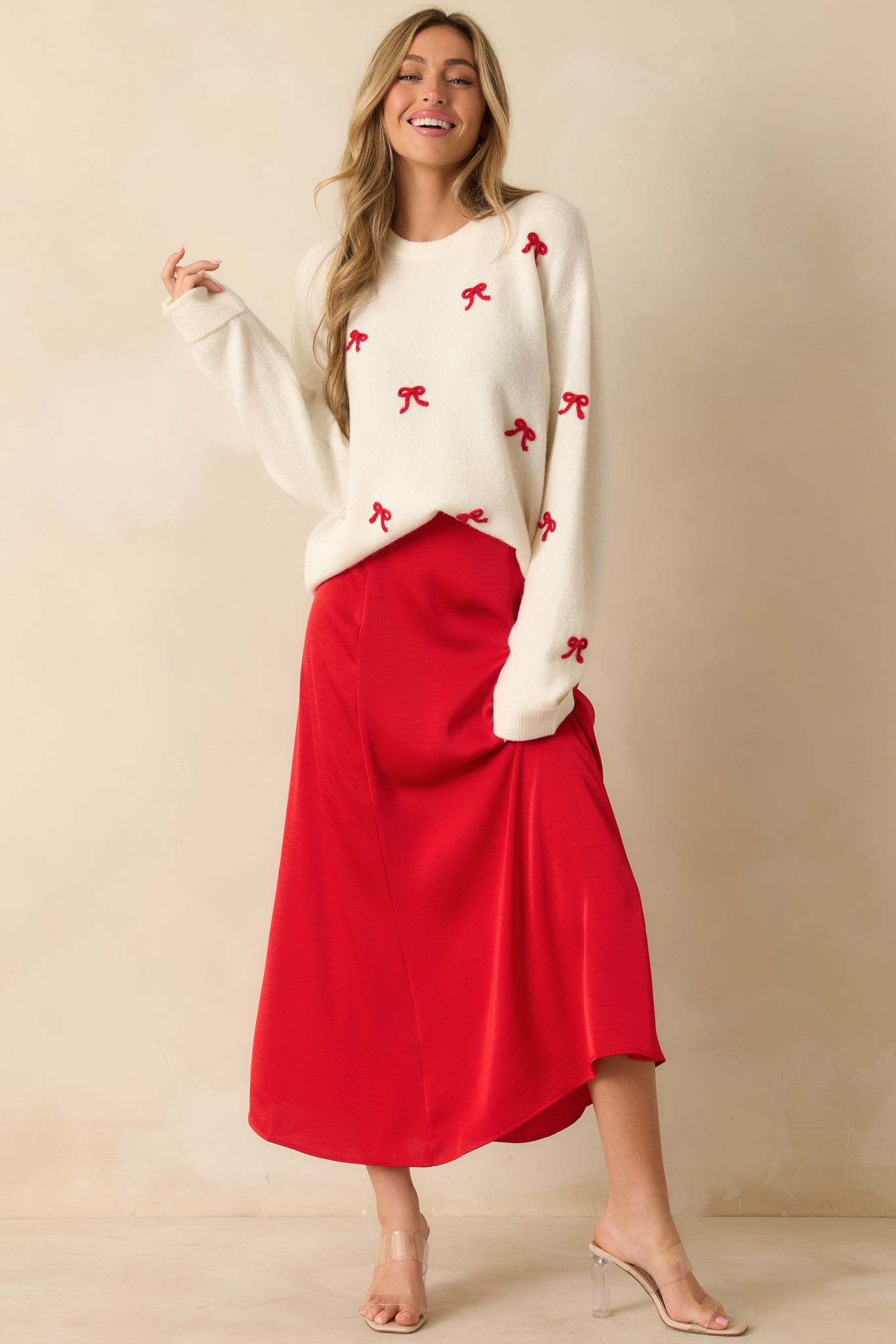 Front view of white soft knit pullover sweater with relaxed fit and embroidered red bow accents across the front.