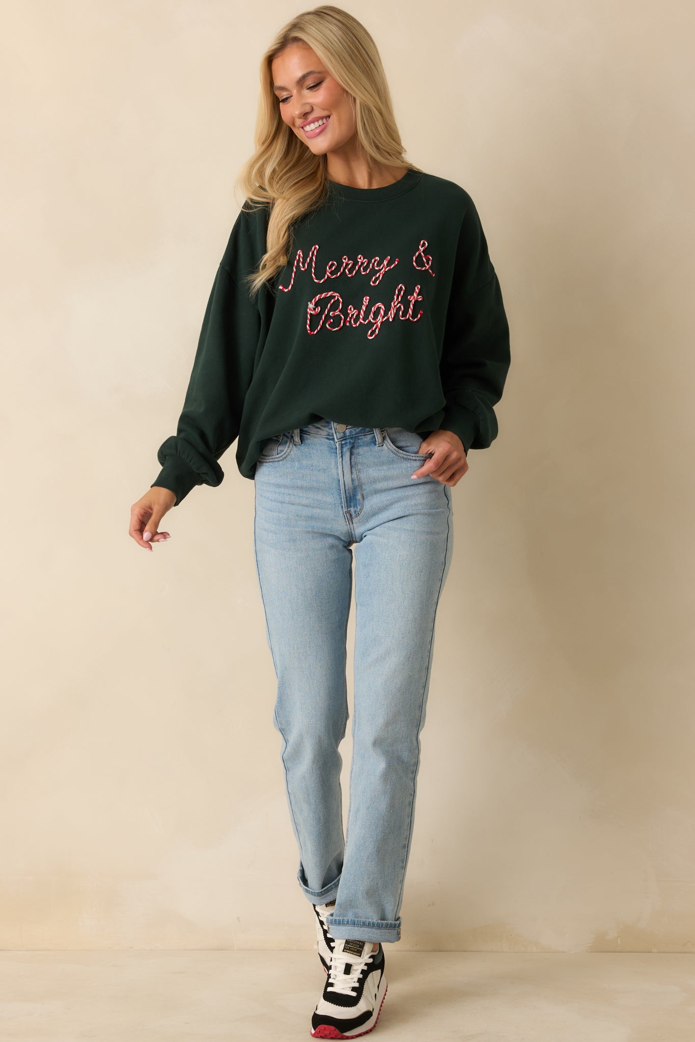 Front view of oversized green sweatshirt with soft fleece fabric, long sleeves, and raised “Merry & Bright” detailing.