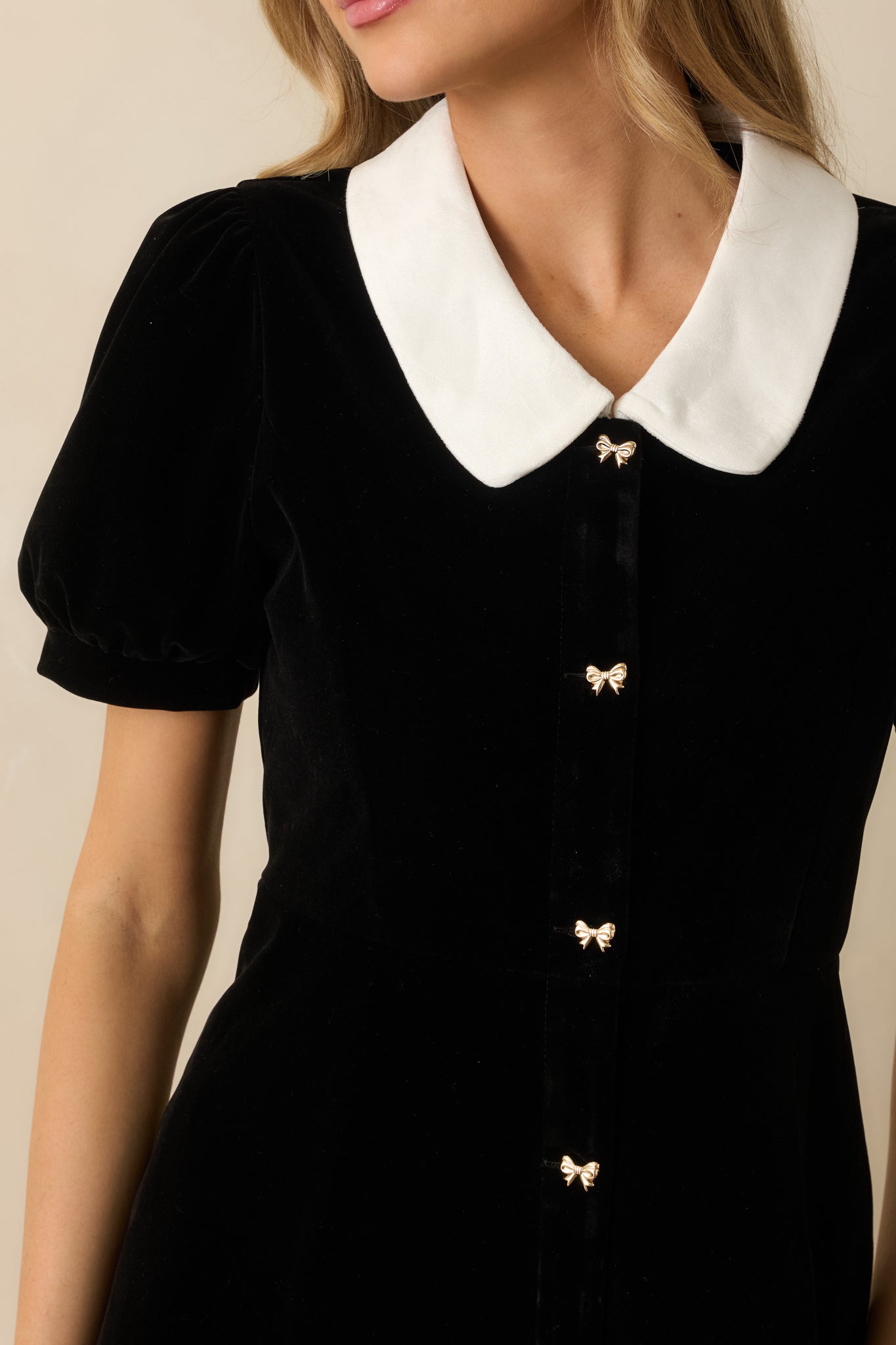 Close-up of the gold bow-shaped button closures and white collar on the black velvet dress.