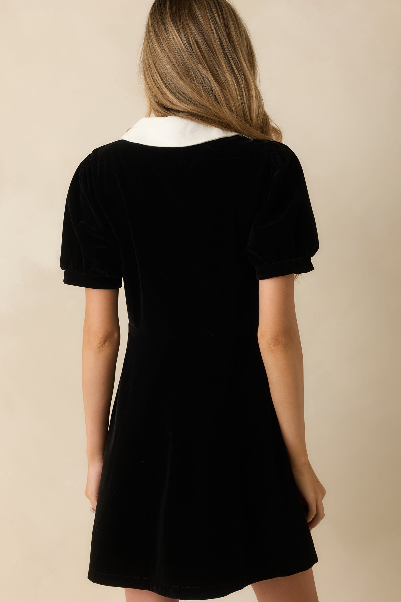 Rear view of the black velvet mini dress showing the fit-and-flare shape and smooth finish.