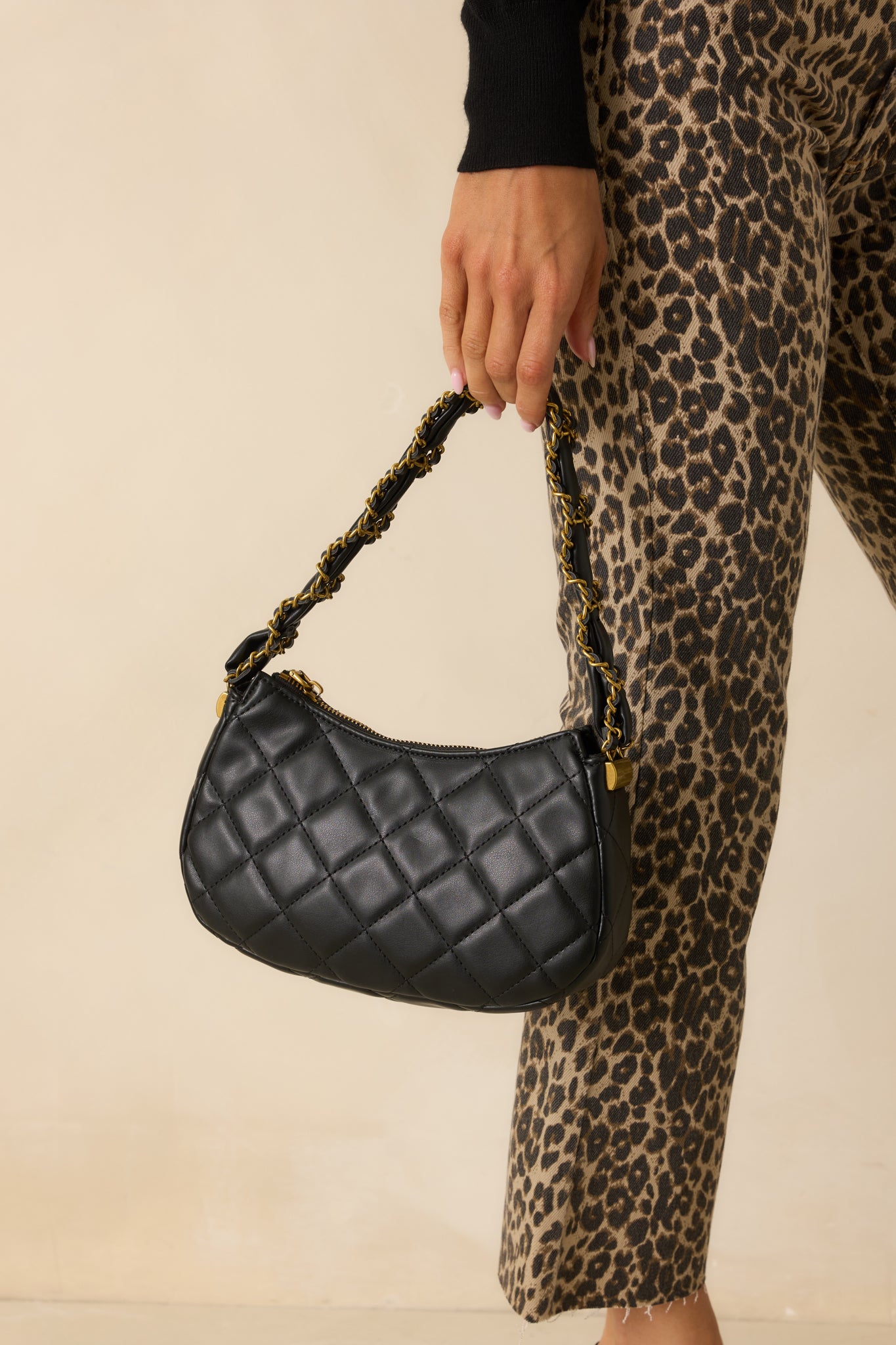 Close view of the black handbag’s braided black and gold chain handle and quilted texture.