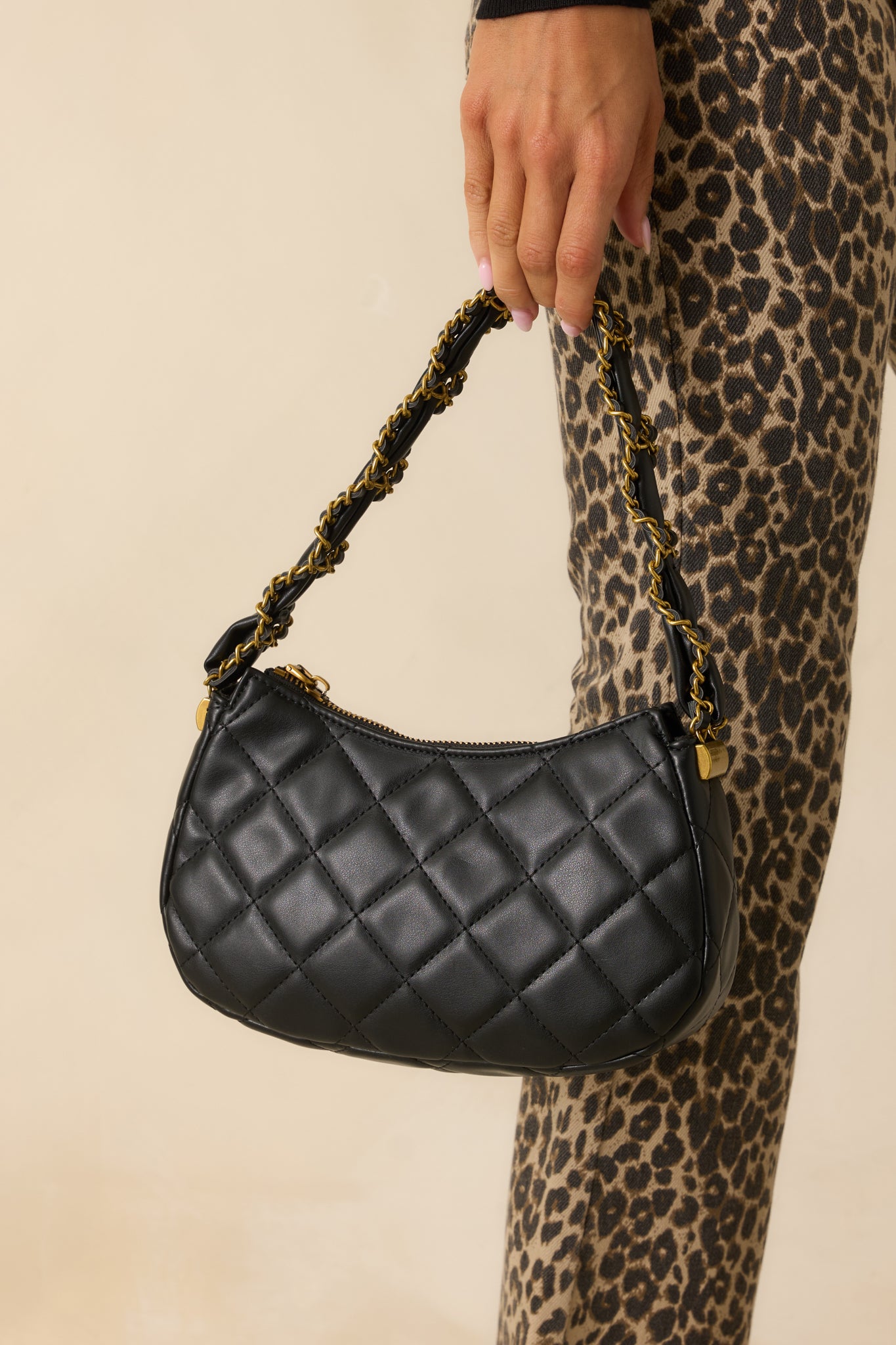 Black faux leather handbag with quilted detailing, a braided black and gold chain handle, and gold zipper closure.