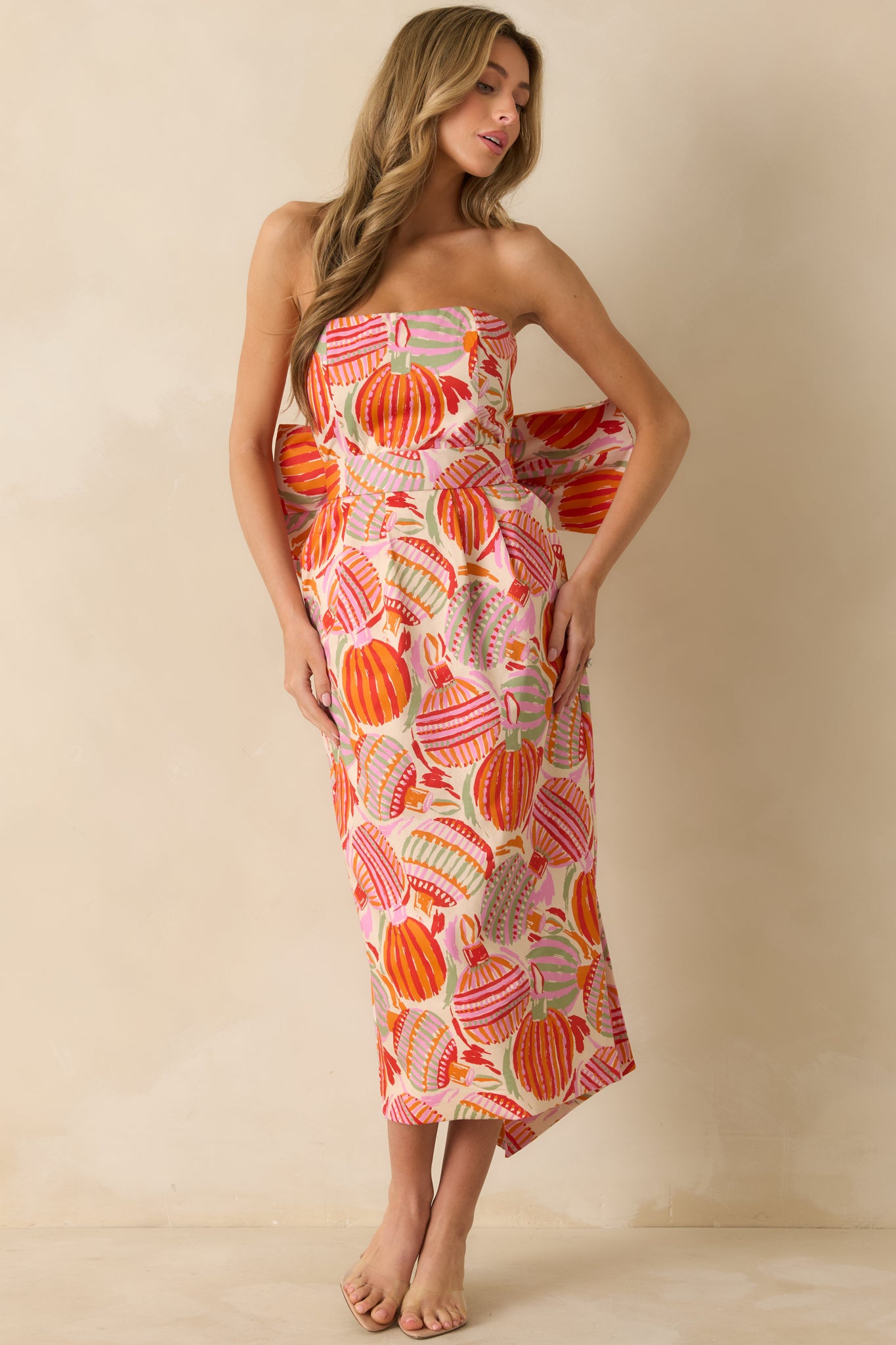 The strapless midi dress shows its pink multicolor print with a bold oversized  bow and structured silhouette.