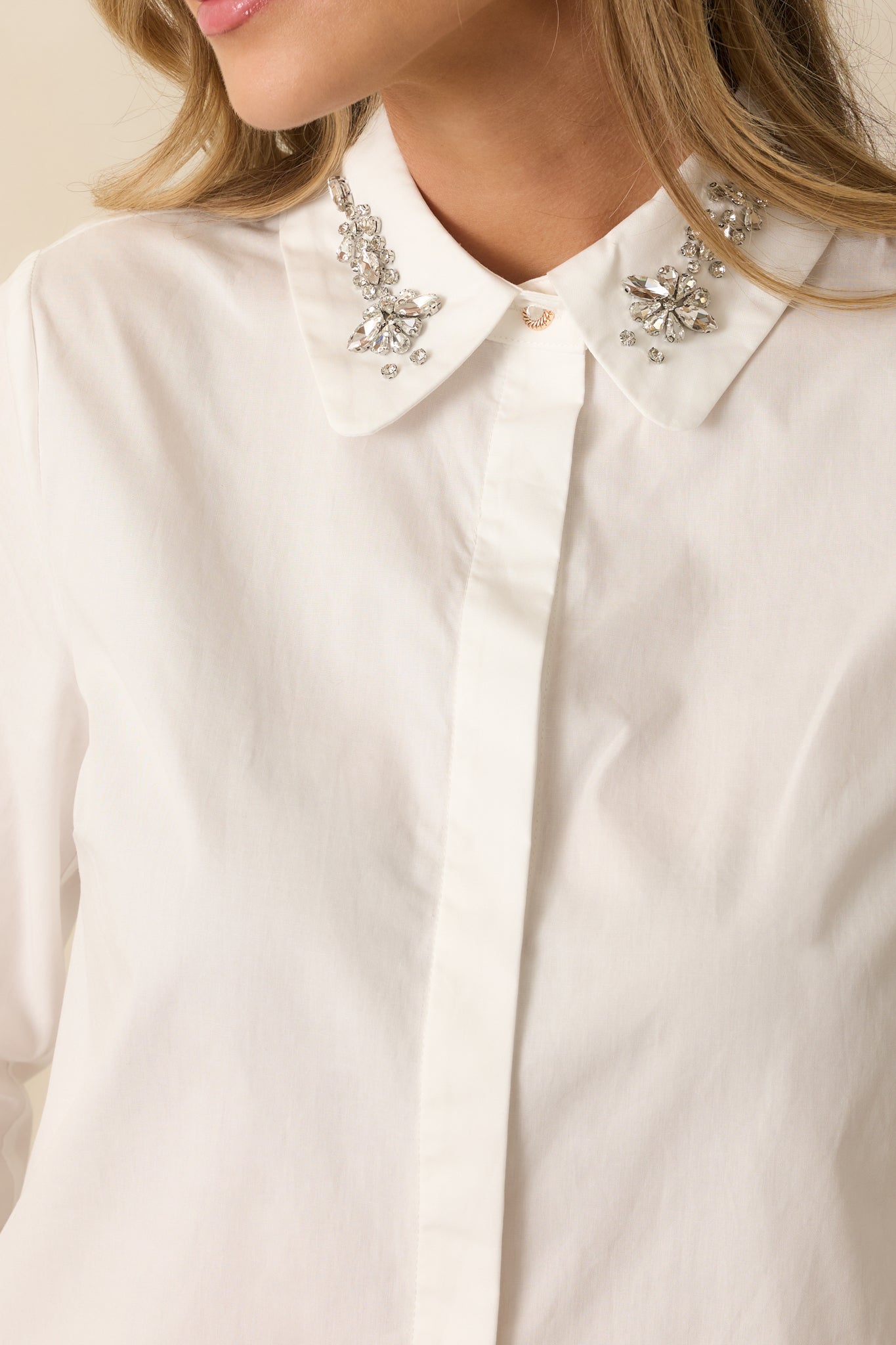 Close-up of the pointed collar with faceted jewel embellishments and smooth woven fabric of the blouse.