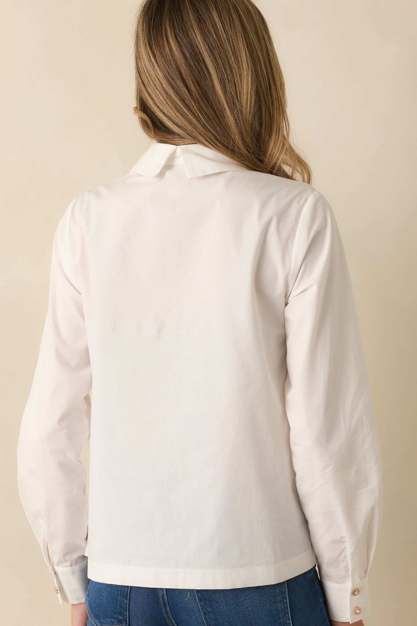 Rear view of the white blouse showing relaxed silhouette, long sleeves, and straight hem.