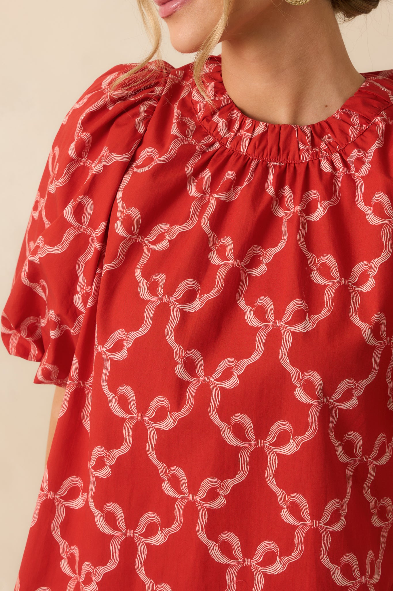 A close view reveals the bow print, gathered neckline stitching, and lightly textured woven cotton.