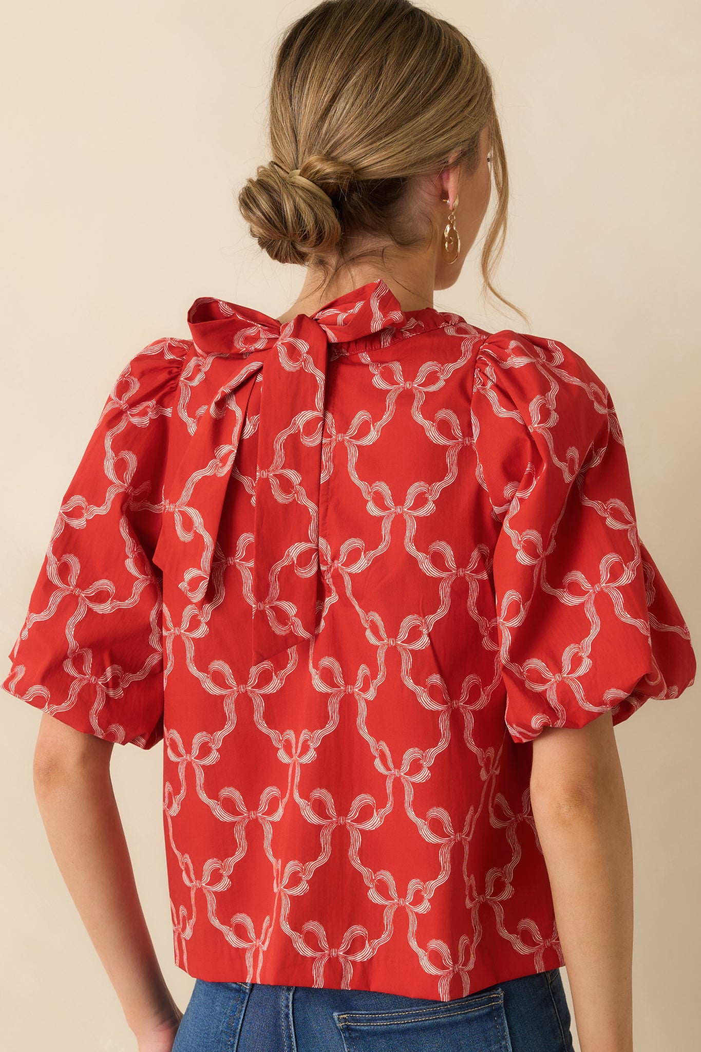 The top at the rear shows the relaxed silhouette and a functional self-tie bow centered against the red bow-printed fabric.