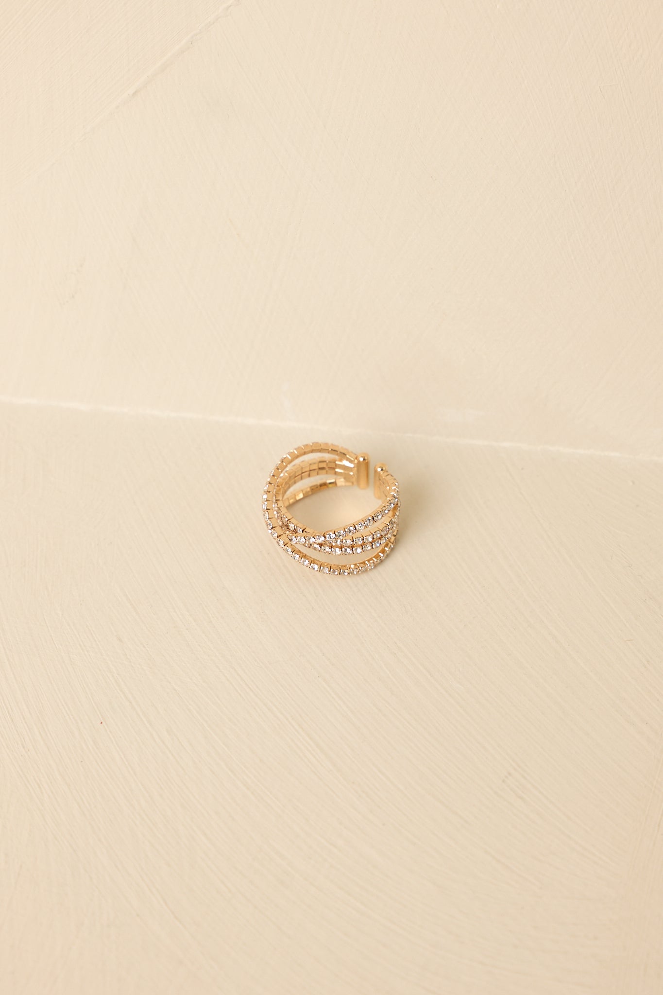 Multi-band gold ring with rows of glittering crystals displayed against a neutral beige background.