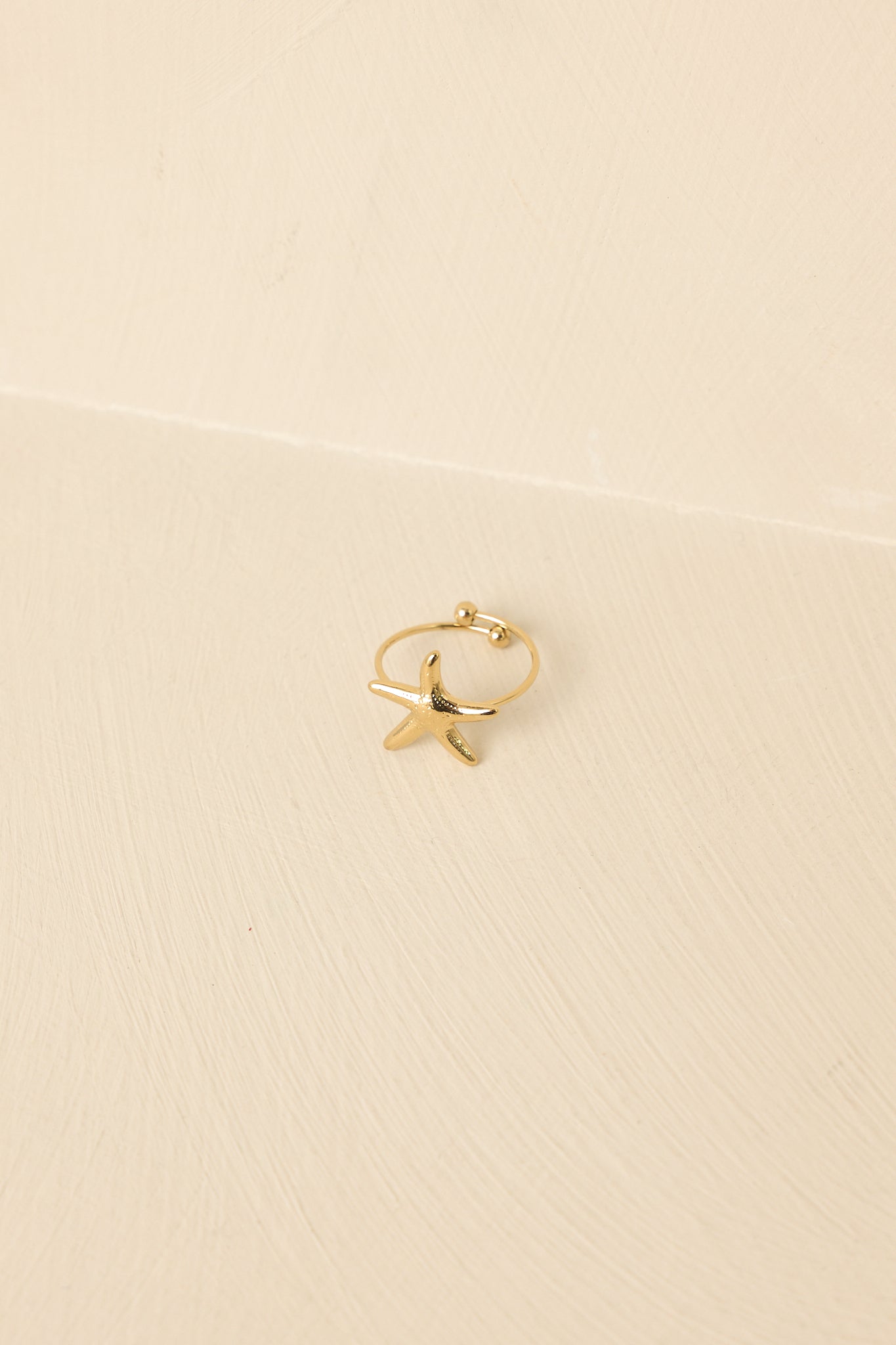 Close-up of gold ring featuring petite starfish motif, smooth polished finish, and thin band