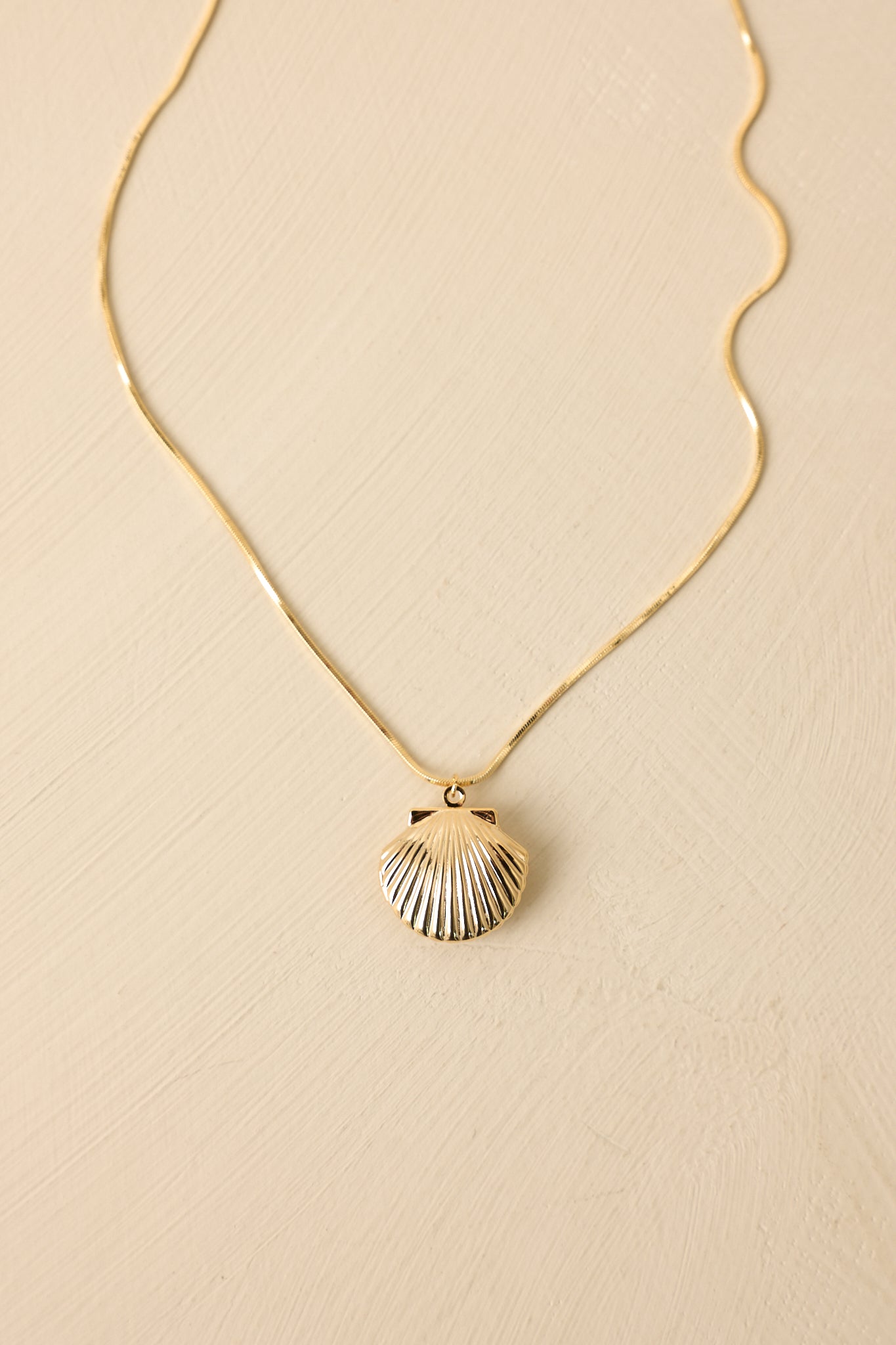 Beige background display showcasing the full necklace with centered shell charm and minimal chain design.