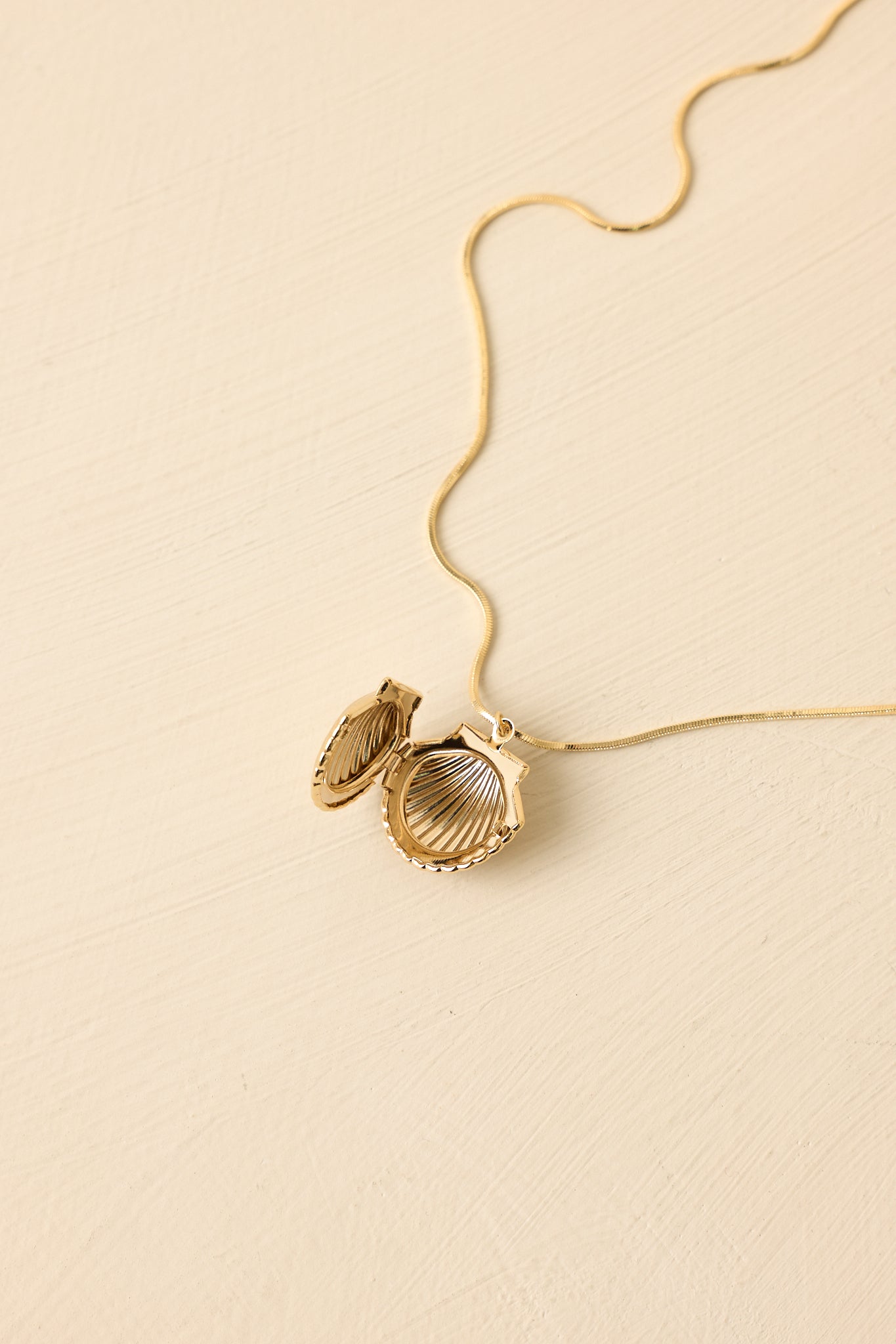 Beige background angled view emphasizing the lightweight chain and dimensional shell pendant shape.