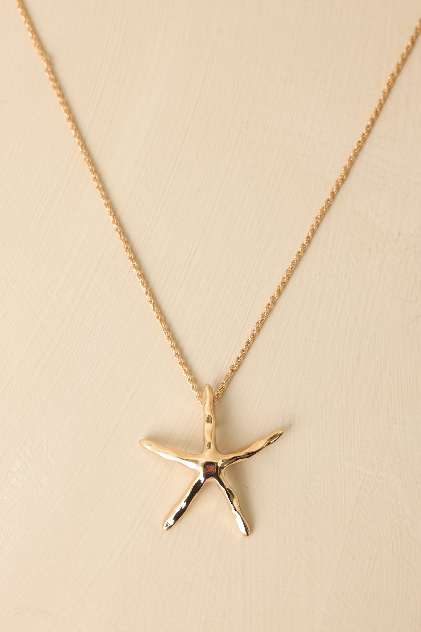 Gold starfish necklace displayed on beige background emphasizing high-shine finish and coastal-inspired charm.