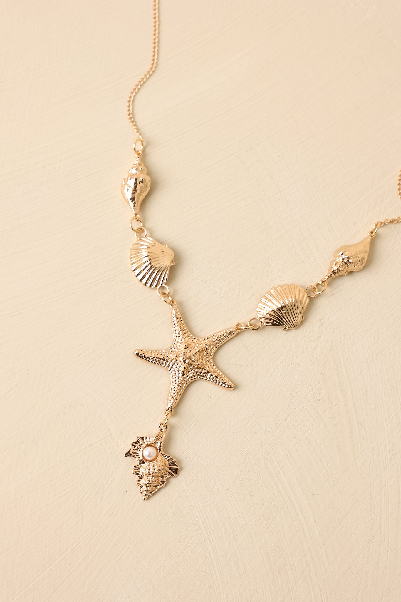 Angled view of coastal charm necklace on beige backdrop highlighting layered pendant design and fine chain.