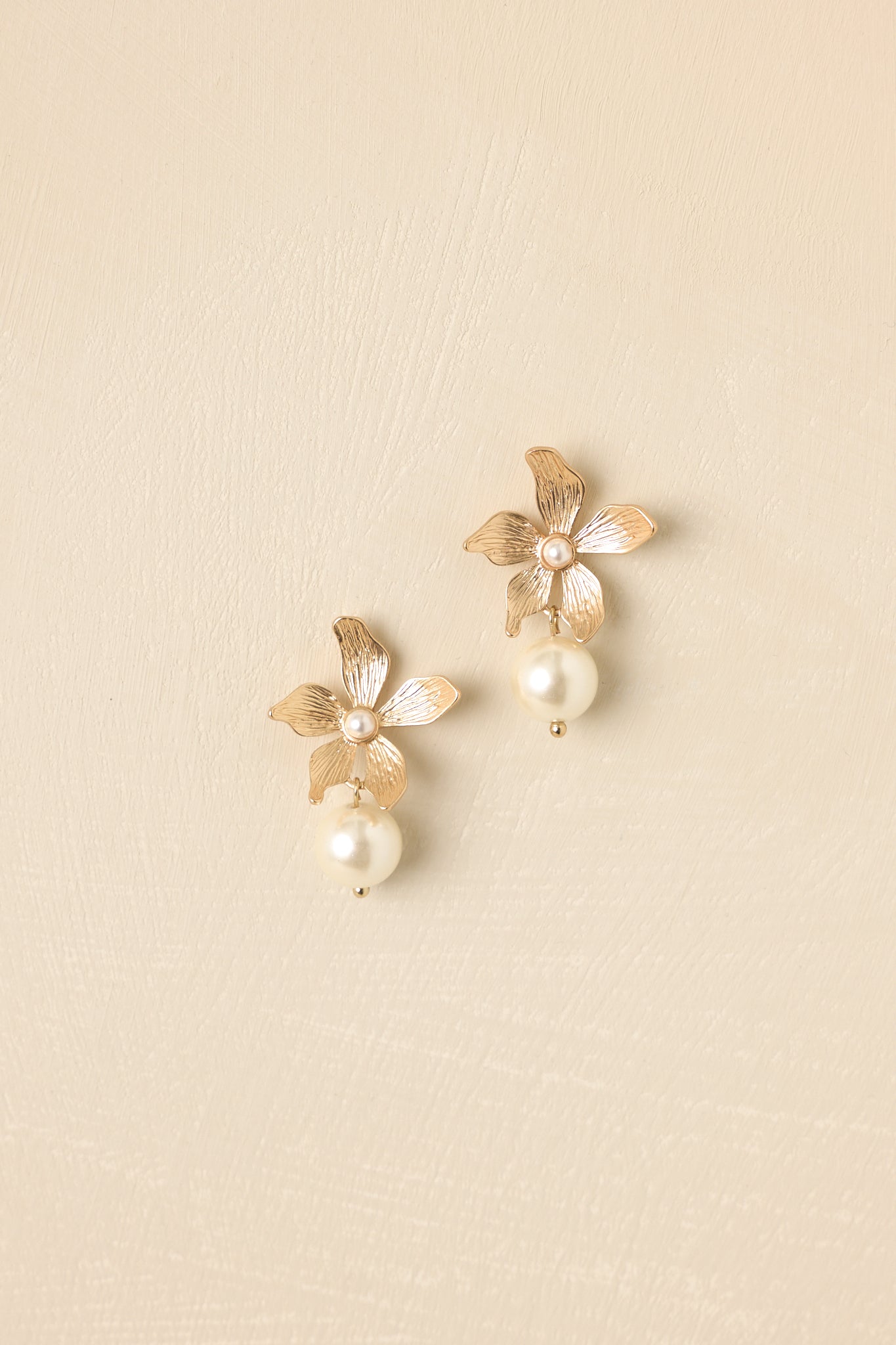Close-up of gold flower and pearl drop earrings highlighting sculpted petal texture and polished luminous pearl for refined elegance.