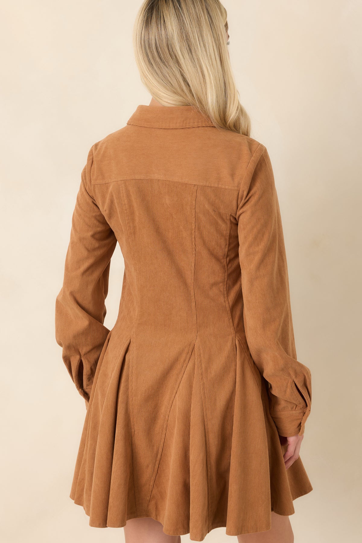 Rear view of the camel corduroy mini dress showing its long sleeves, defined waist seams, and flared paneled skirt.