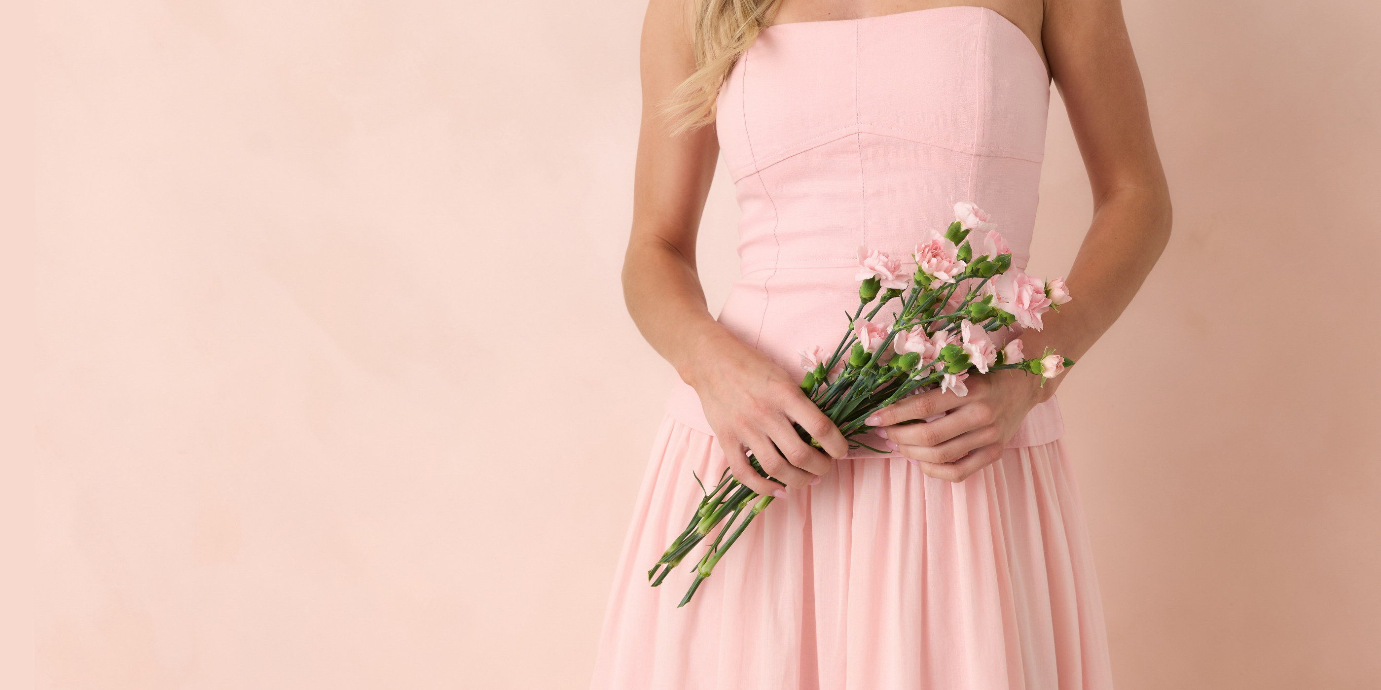 Person wearing a strapless pink dress holding flowers against a beige background