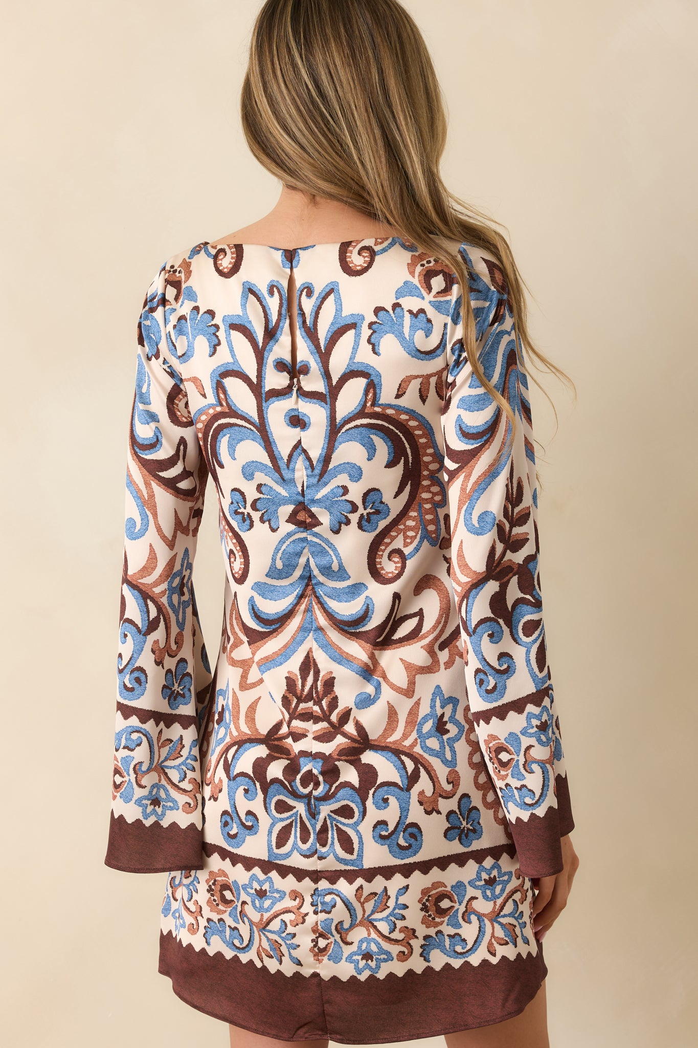 Back view of the mini dress showing the hidden back zipper closure, flare sleeves, and full paisley pattern.