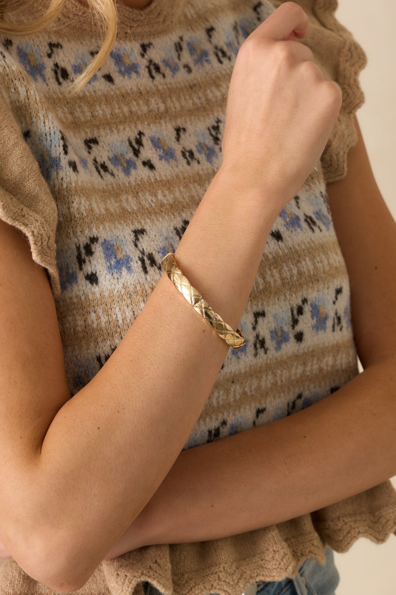 Cropped view of the gold bangle-style bracelet showing the embossed crisscross detail and elastic interior.