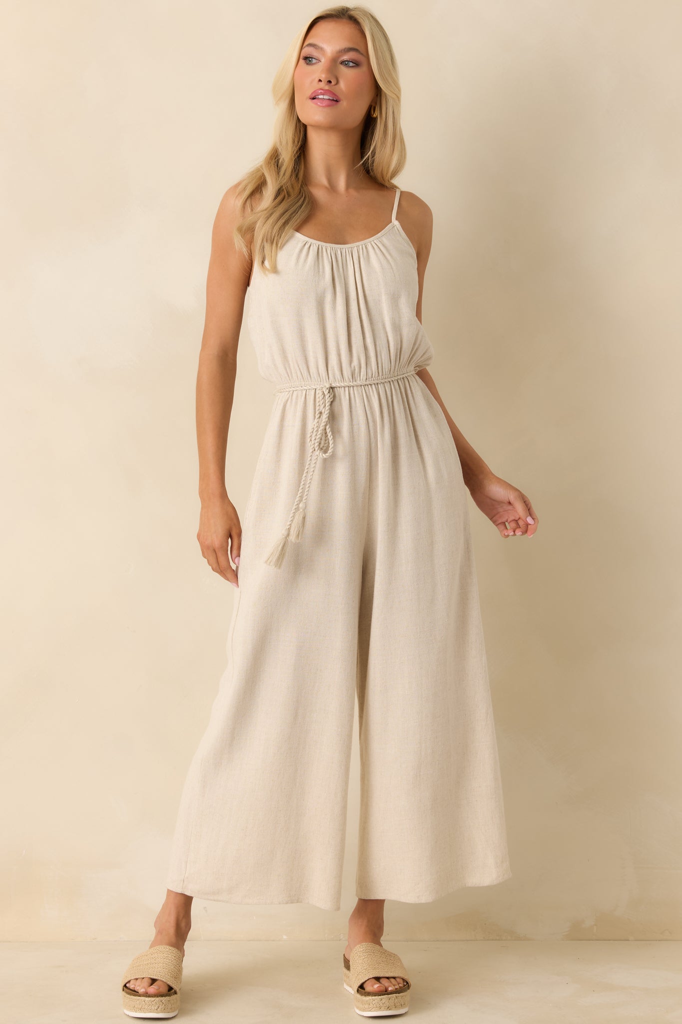 Front view of beige jumpsuit emphasizing wide-leg flow, functional pockets, and scooped neckline.