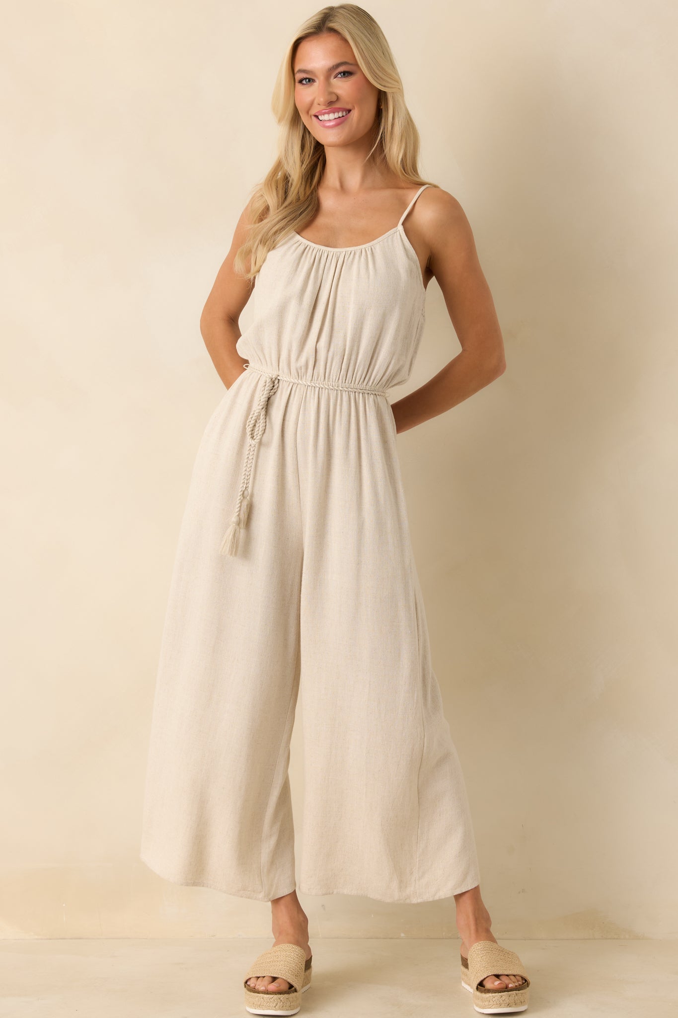 Front view of beige jumpsuit showing scoop neckline, adjustable straps, and wide-leg design.