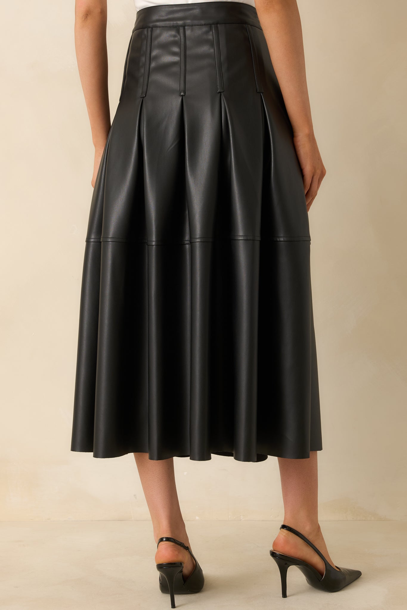Rear view of the black faux leather midi skirt showing the full A-line drape and smooth waistband.