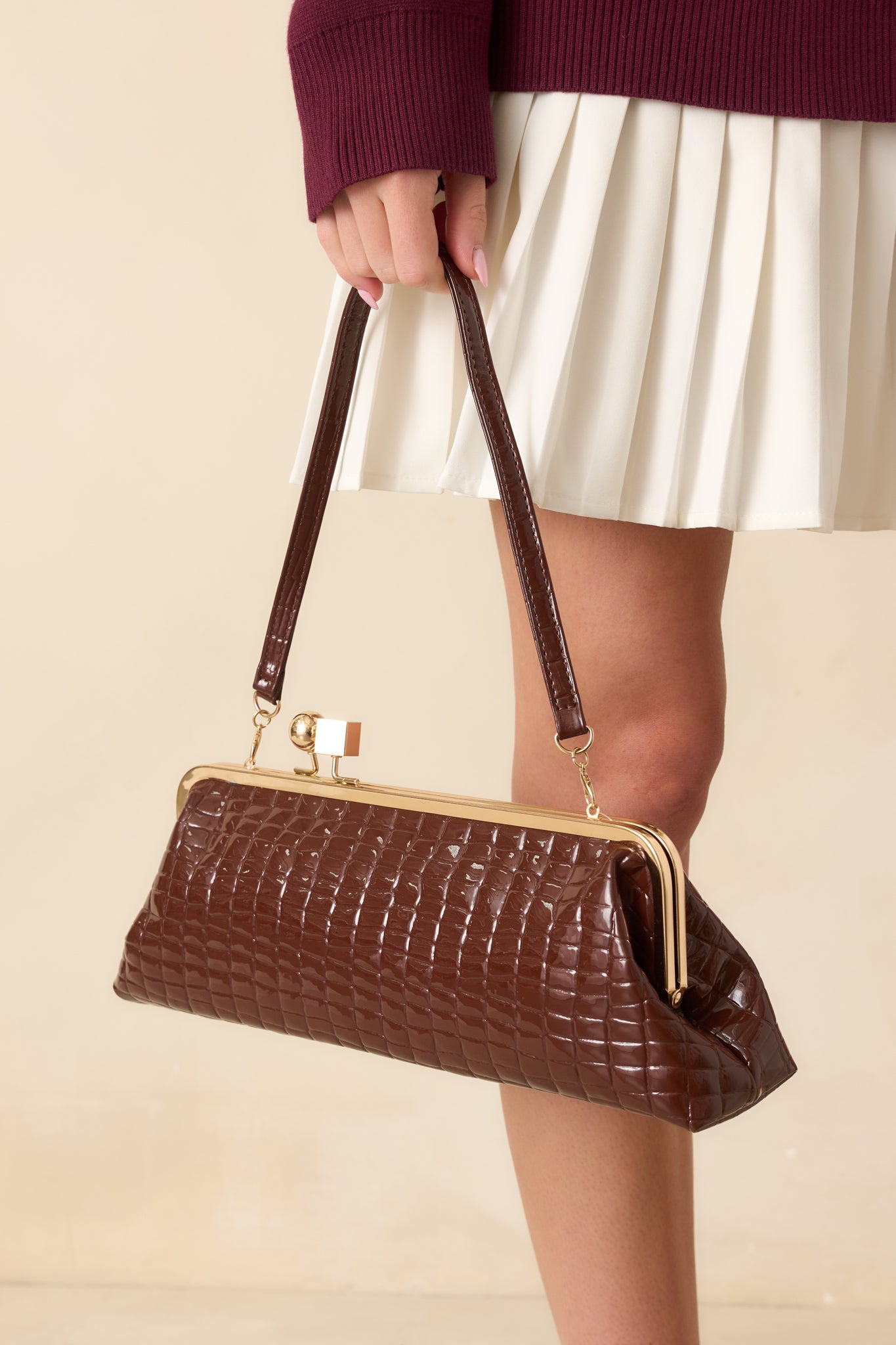 Full body front view of brown croc-embossed clutch showing gold kiss-lock frame and rectangular silhouette.