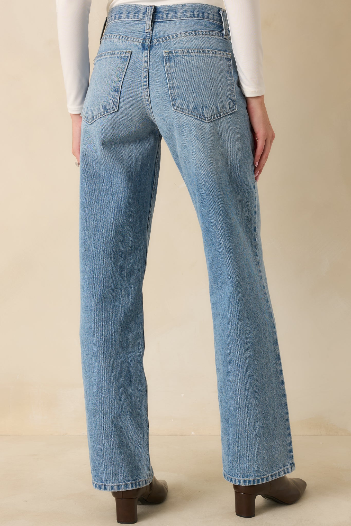 Rear view showing back pockets, high waist, and straight leg fit of light wash jeans.