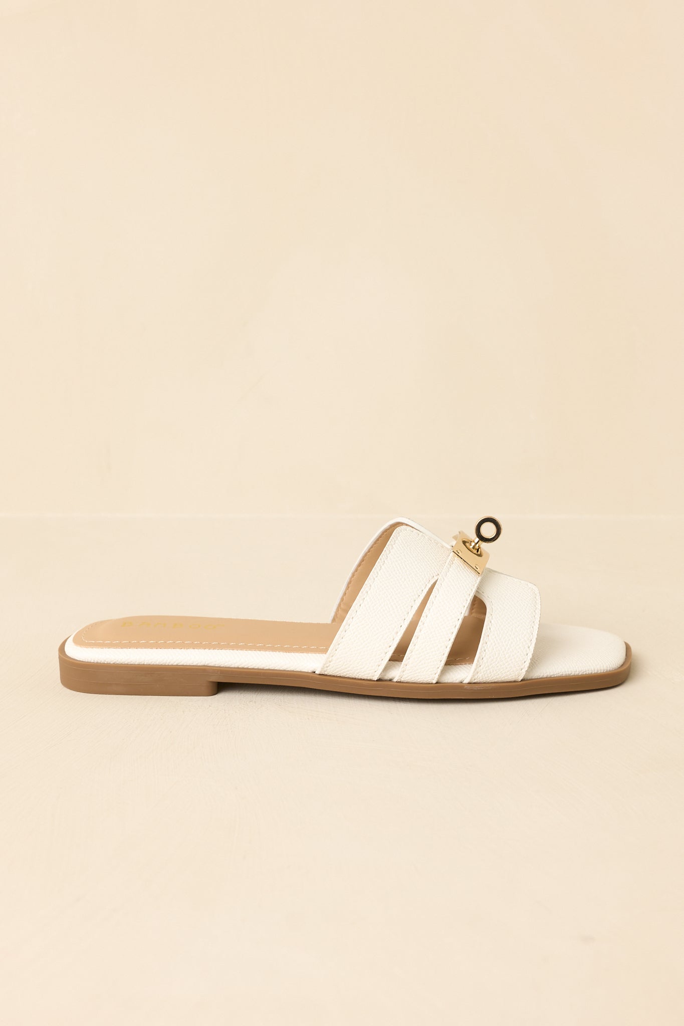 Side view of flat white slide sandals on beige background showing slip-on silhouette and strap details.