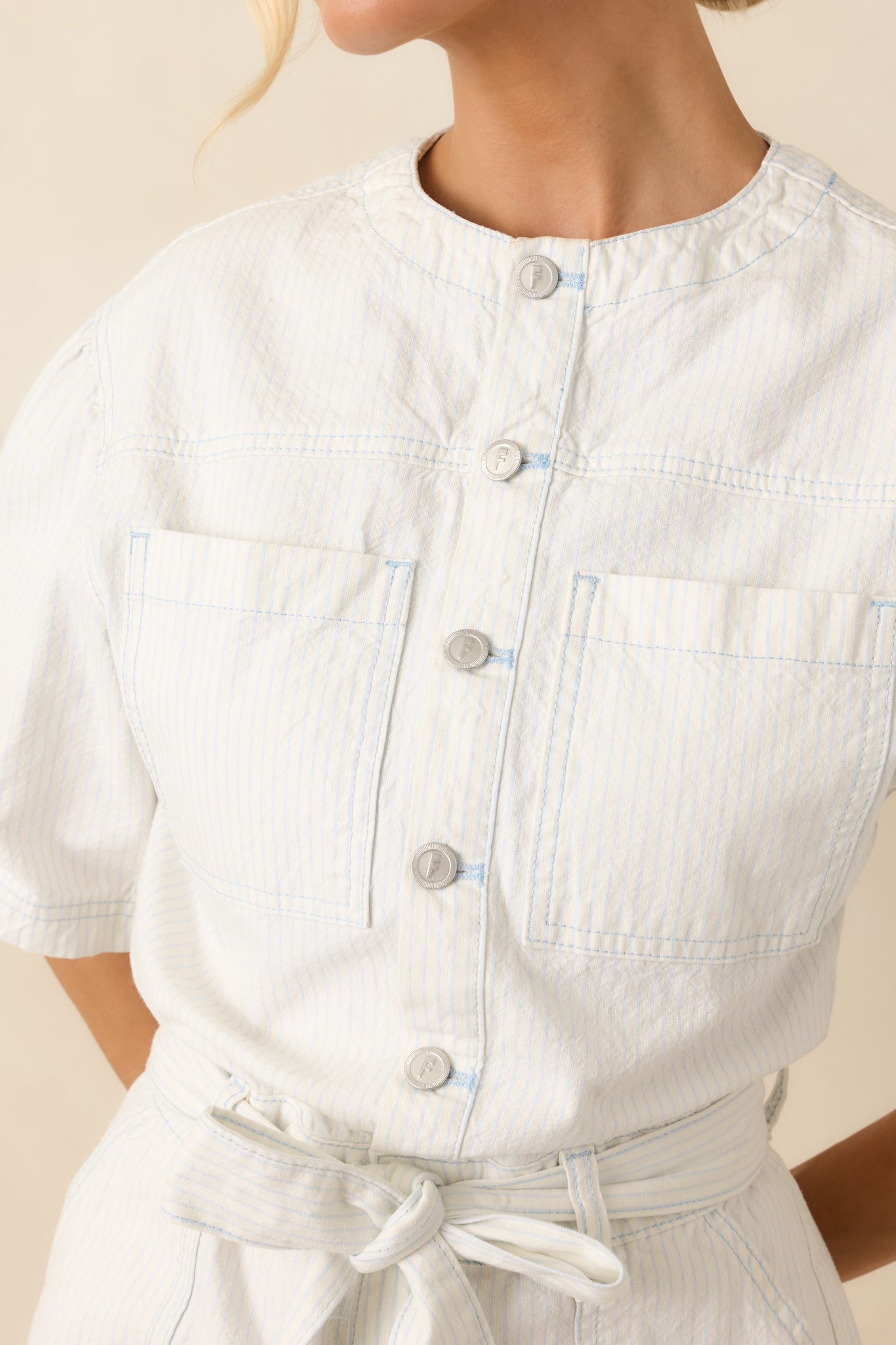 Detailed view of ivory and sky blue striped romper showcasing fabric texture, button-front closure, and stitching details.