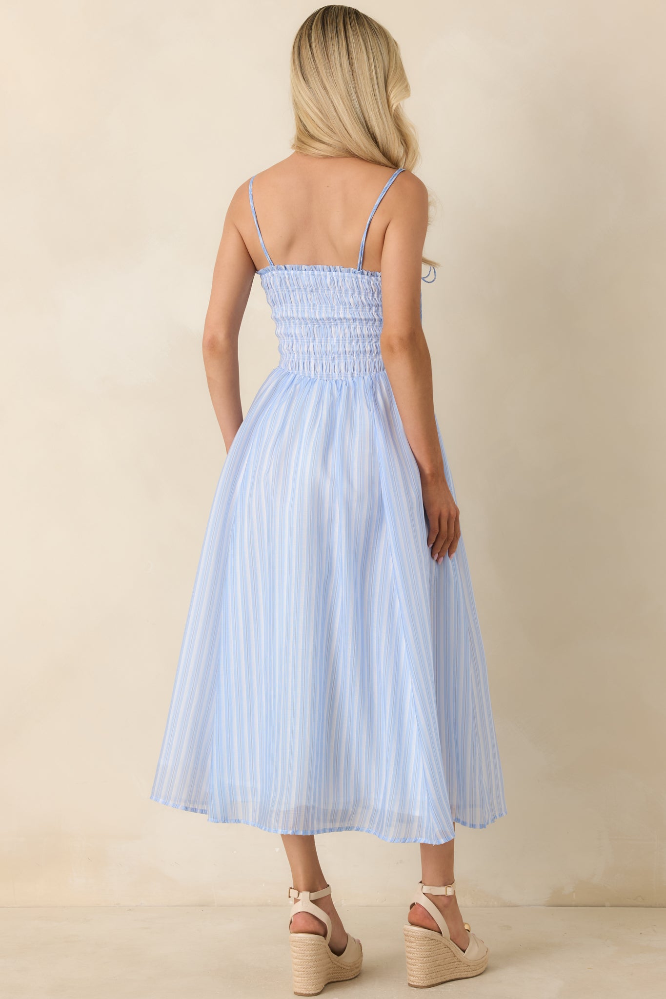 Back view of the light blue and white striped midi dress featuring a smocked bodice, adjustable tie straps, and a flowy midi-length skirt.