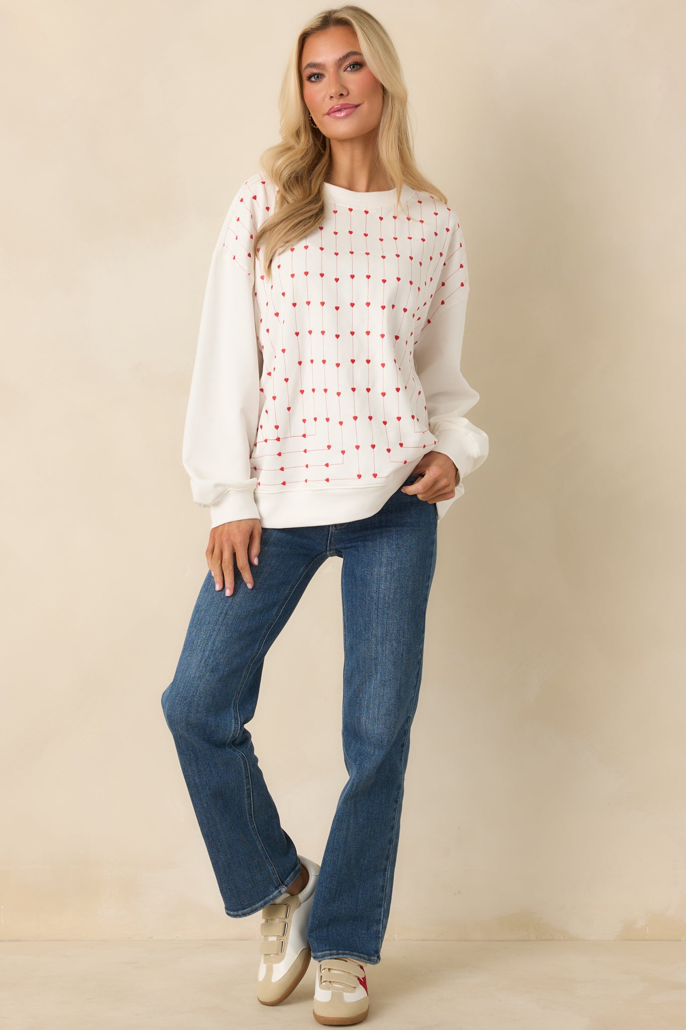 Soft all-cotton white sweatshirt with long sleeves, ribbed cuffs, and vertical embroidered hearts forming a subtle repeated design on the front.