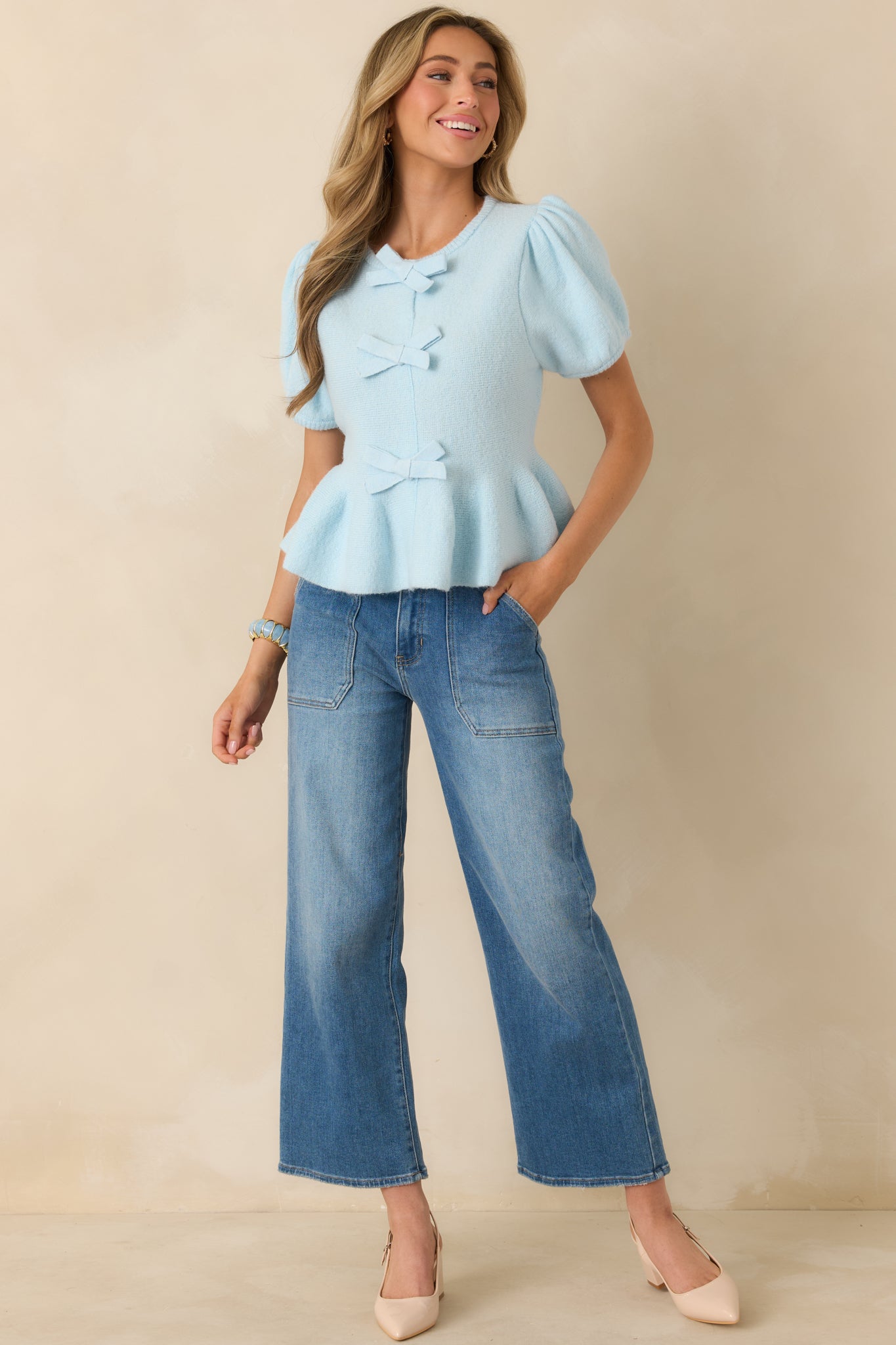 Light blue knit top with rounded neckline, short puff sleeves, fitted bodice, and a soft peplum hem.