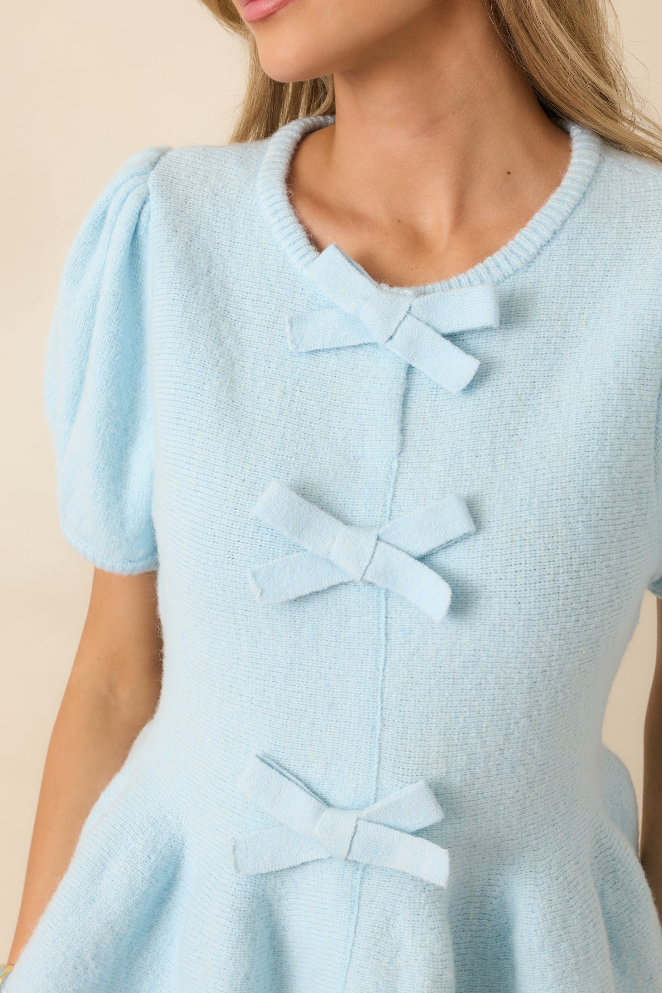 Detailed look at a decorative bow on a light blue knit top, showing knit texture and soft stretch fabric.