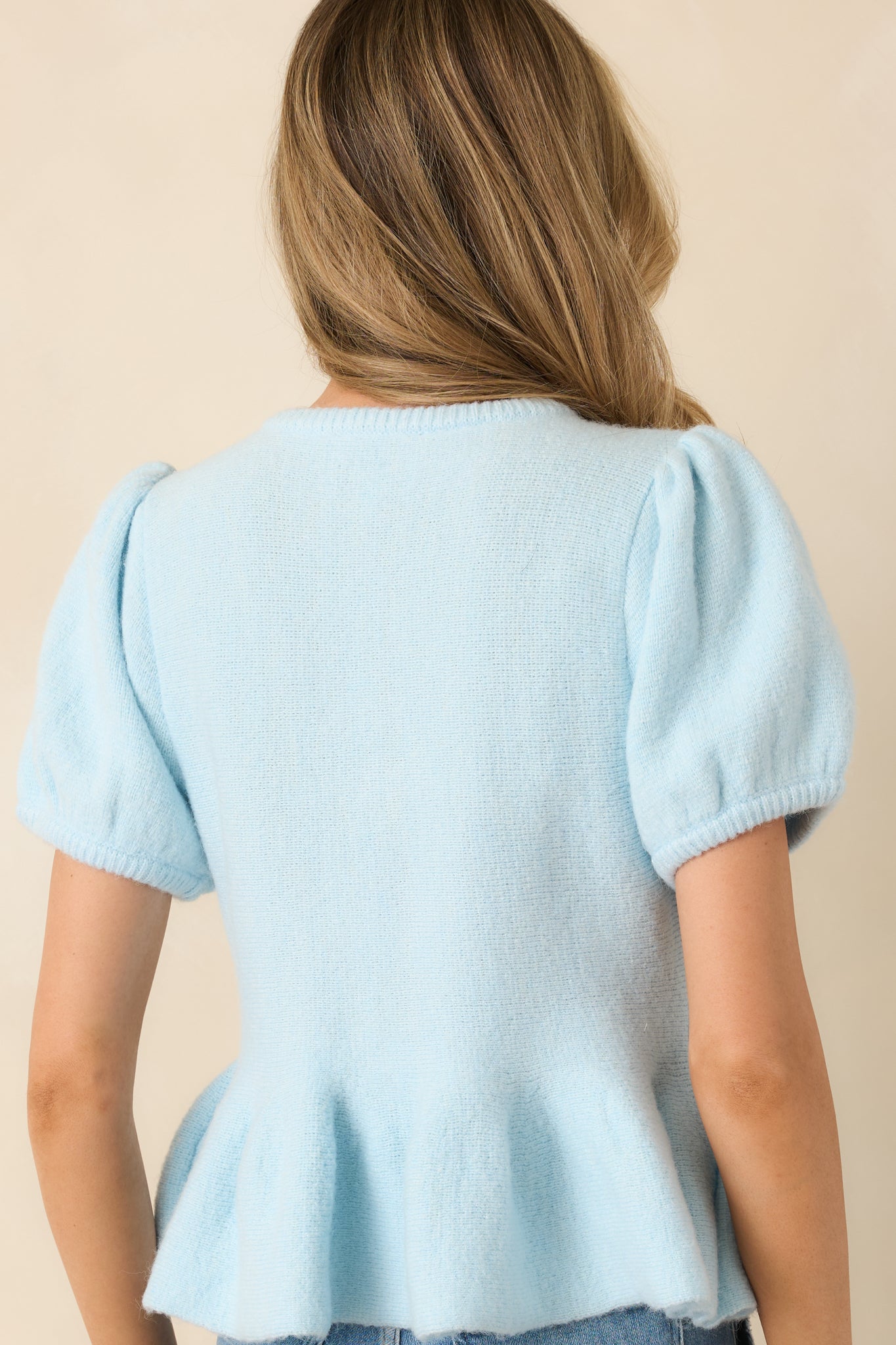 Rear view of a light blue knit top with fitted bodice, rounded neckline, short puff sleeves, and peplum hem.