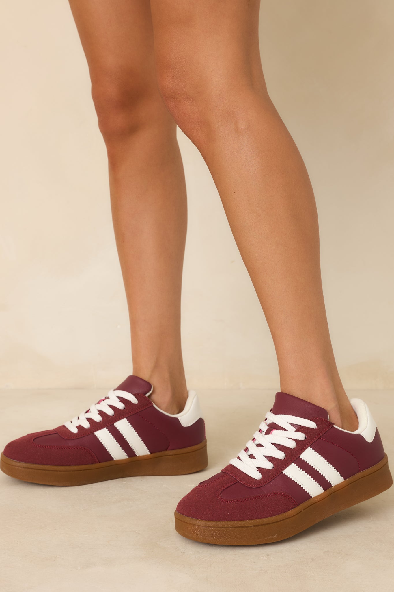 Burgundy sneakers focusing on the white contrast stripes and soft suede texture