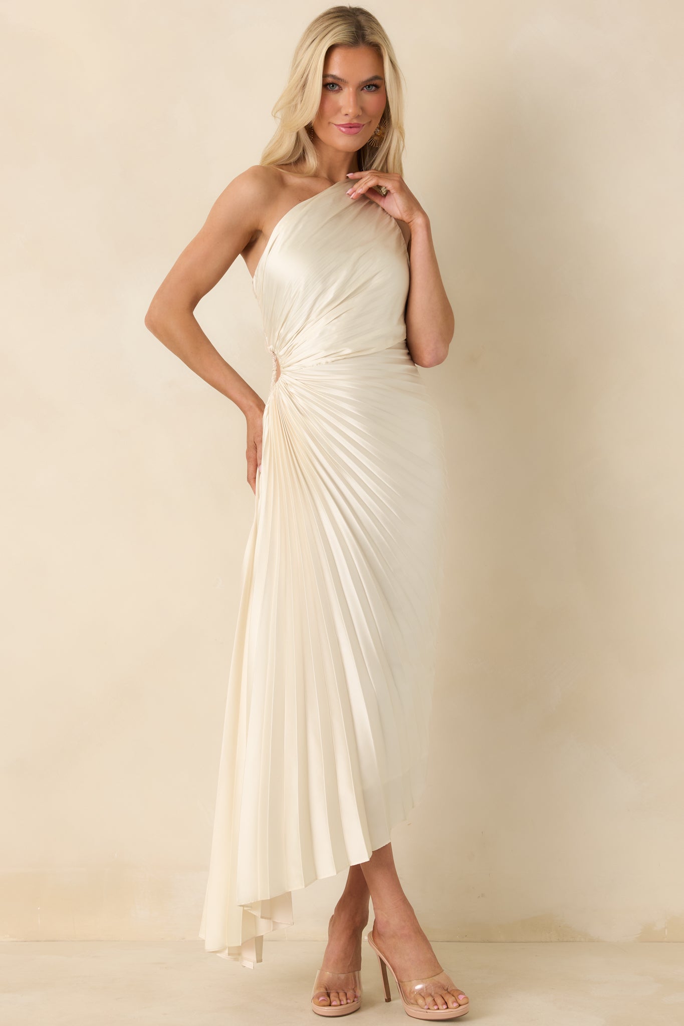 Ivory pleated maxi dress with a fitted top, small side cutout, and asymmetric hem creating elegant movement.