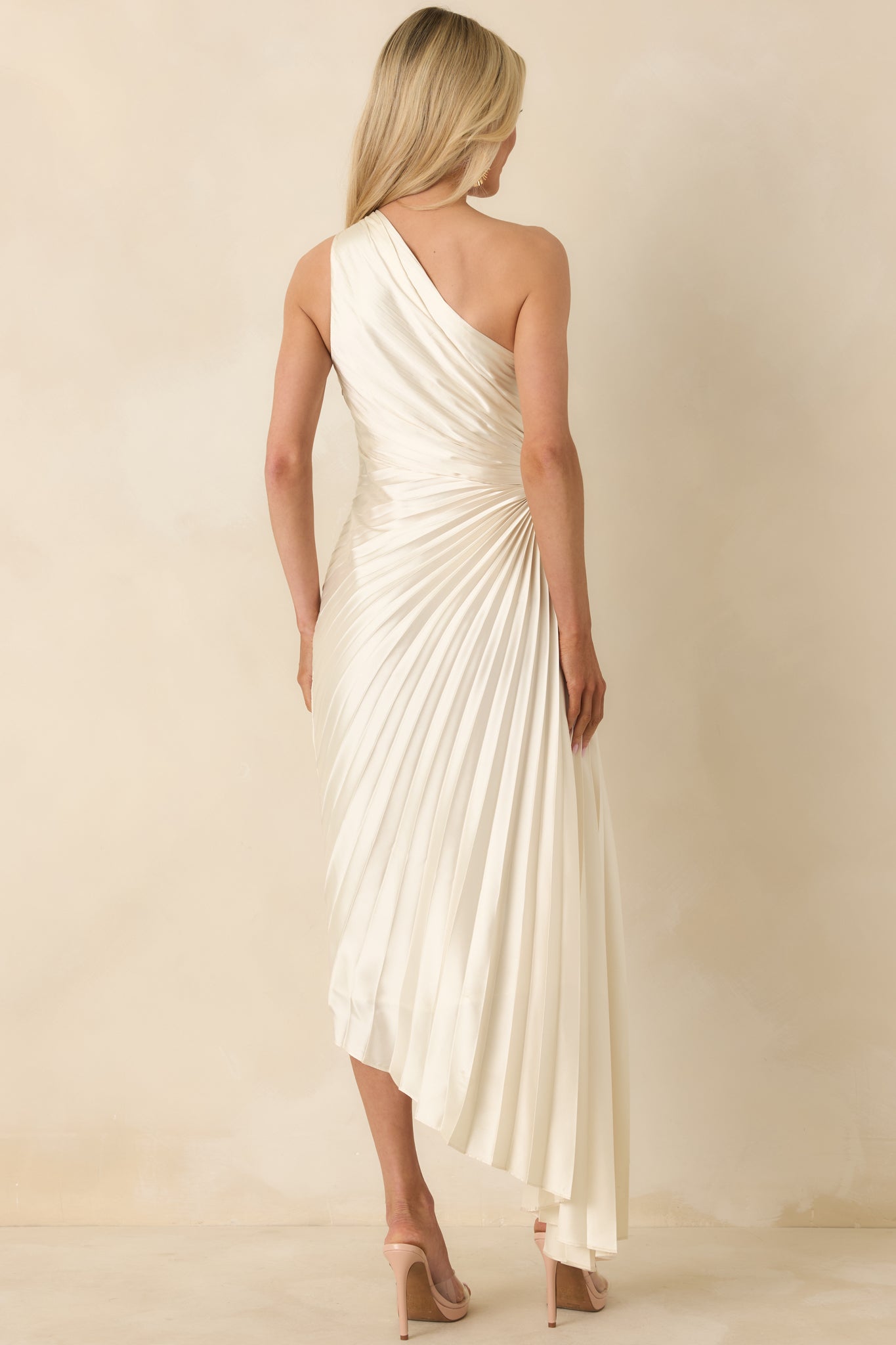 Rear view of the light ivory maxi dress displaying the pleated skirt, asymmetric hem, and concealed back zipper.