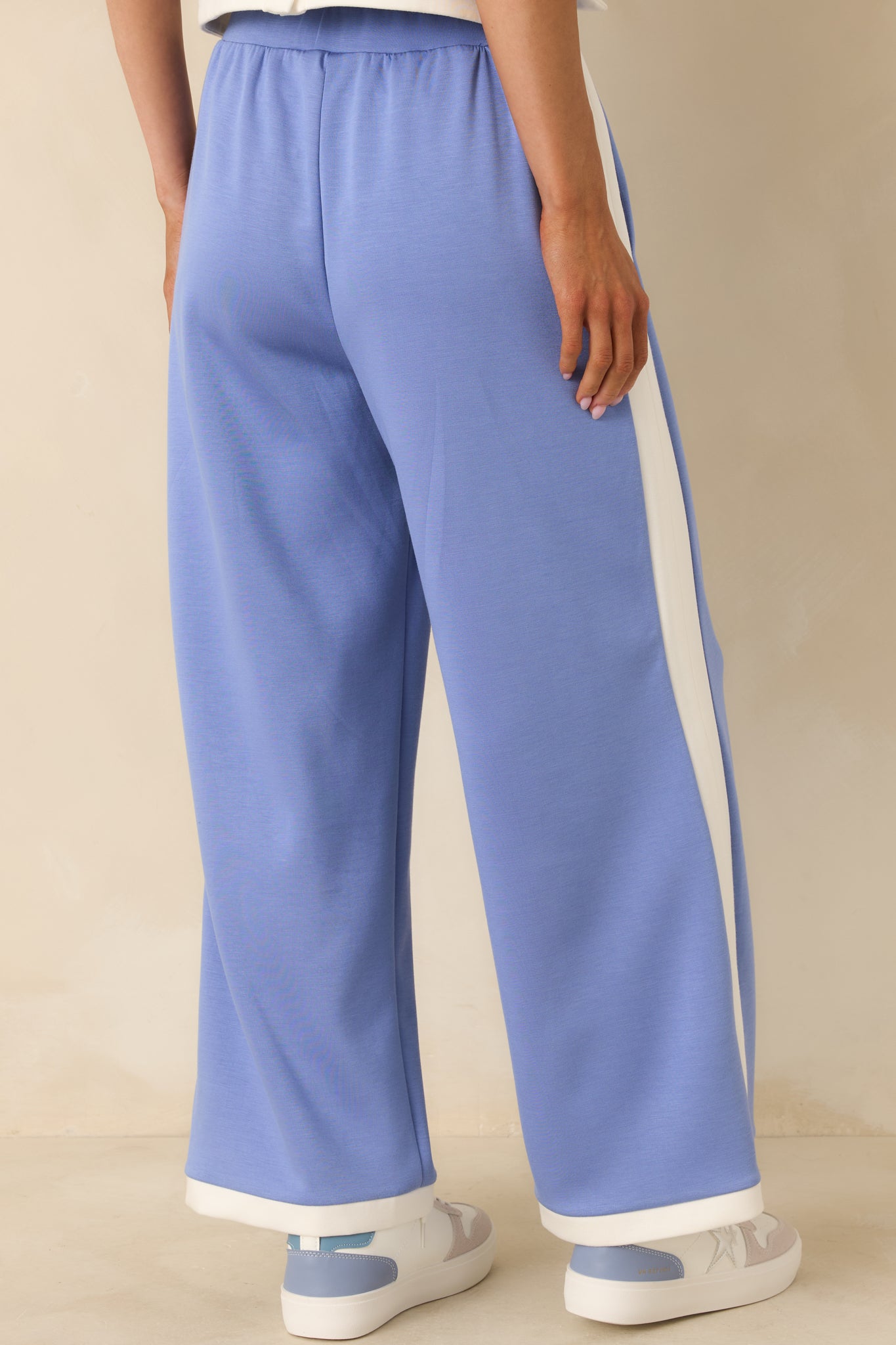 Periwinkle wide-leg knit pants with elastic waistband, contrast side trim, and hem shown from the rear.