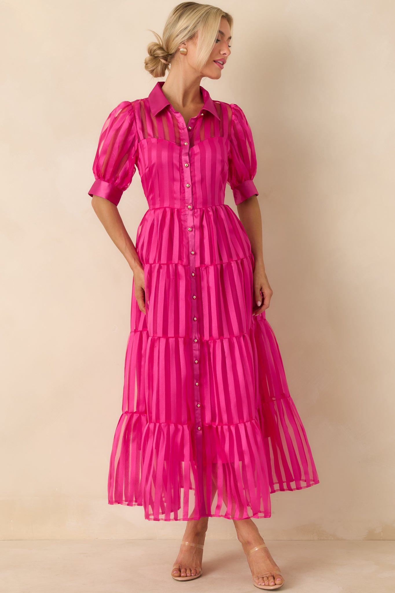 Fuchsia pink maxi dress with short puff sleeves, collared neckline, button closure, and tiered skirt with fluid motion.
