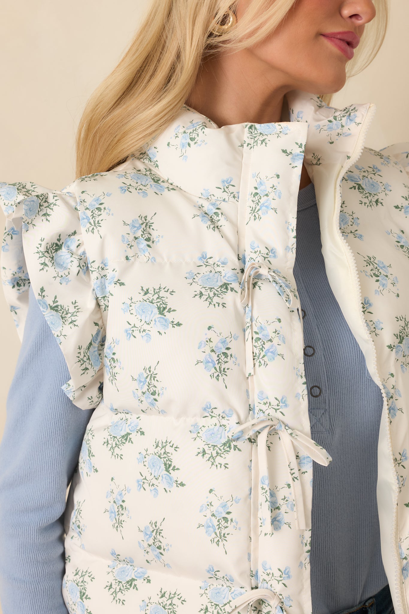 Tight view of the ivory vest fabric showing the quilted blue floral pattern and frilled arm trim for subtle detail.
