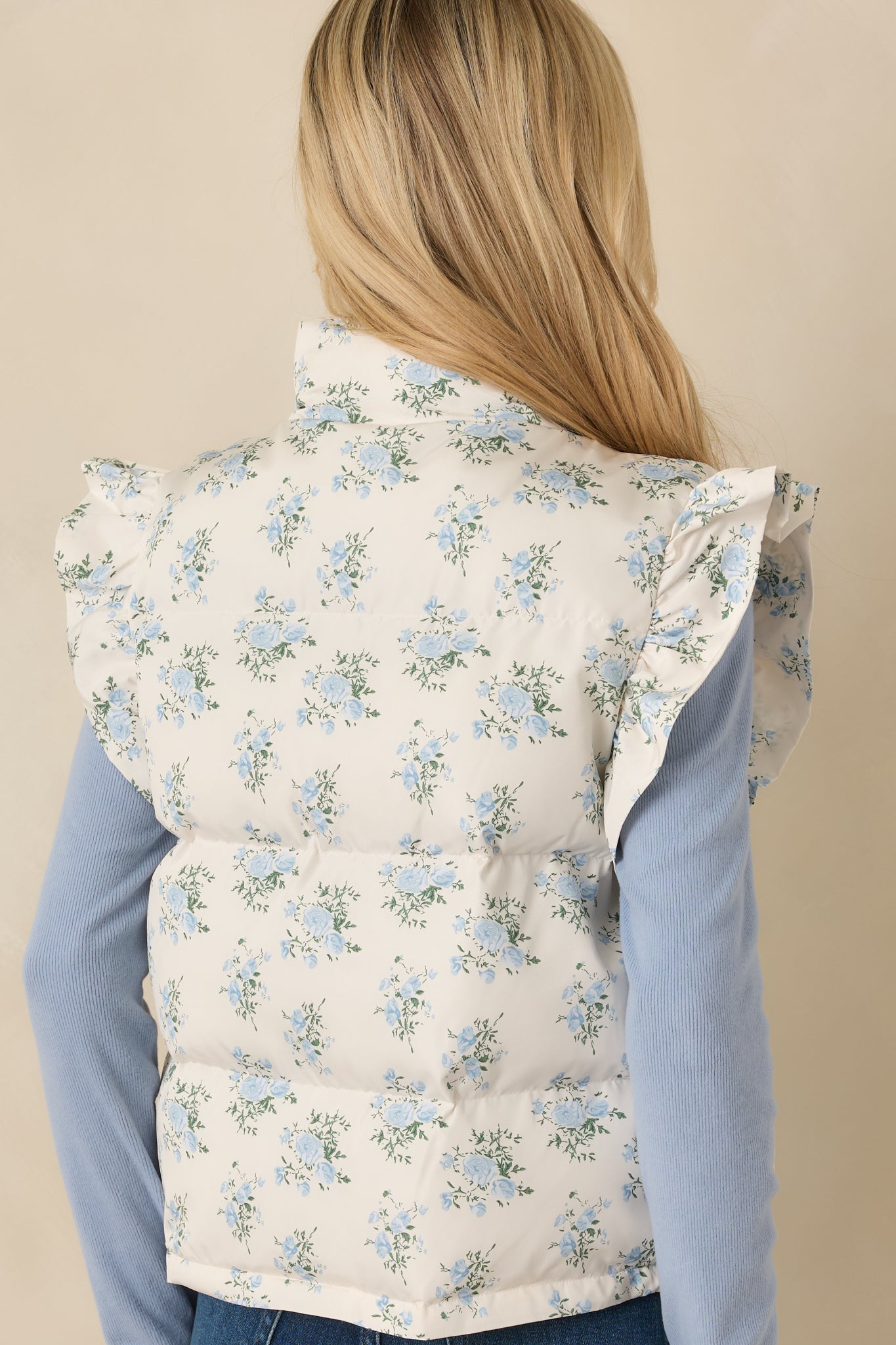 Rear of the ivory puffer vest showing continuous blue floral quilted pattern and smooth, lightly padded back panel.
